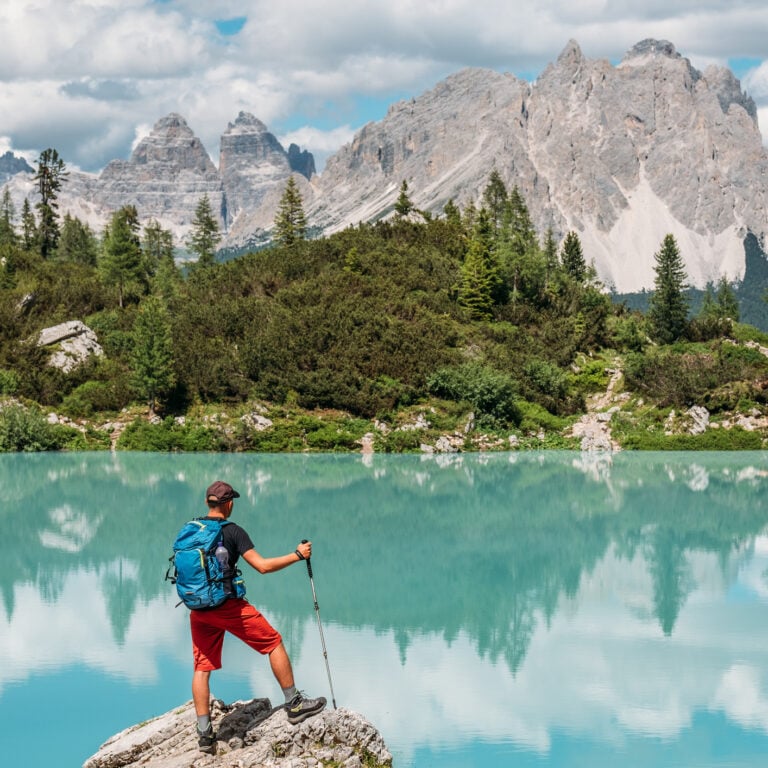 Backpacker with backpack enjoying the turquoise Lago di Sorapiss 1,925m altitude (mountain lake) view as he has mountain walk in Dolomite Mountains, Italy. Active people in nature concept.