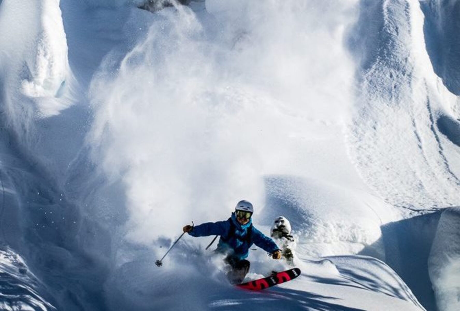 A backcountry skier skiing over powder-covered boulders, near Purcell Mountain Lodge.