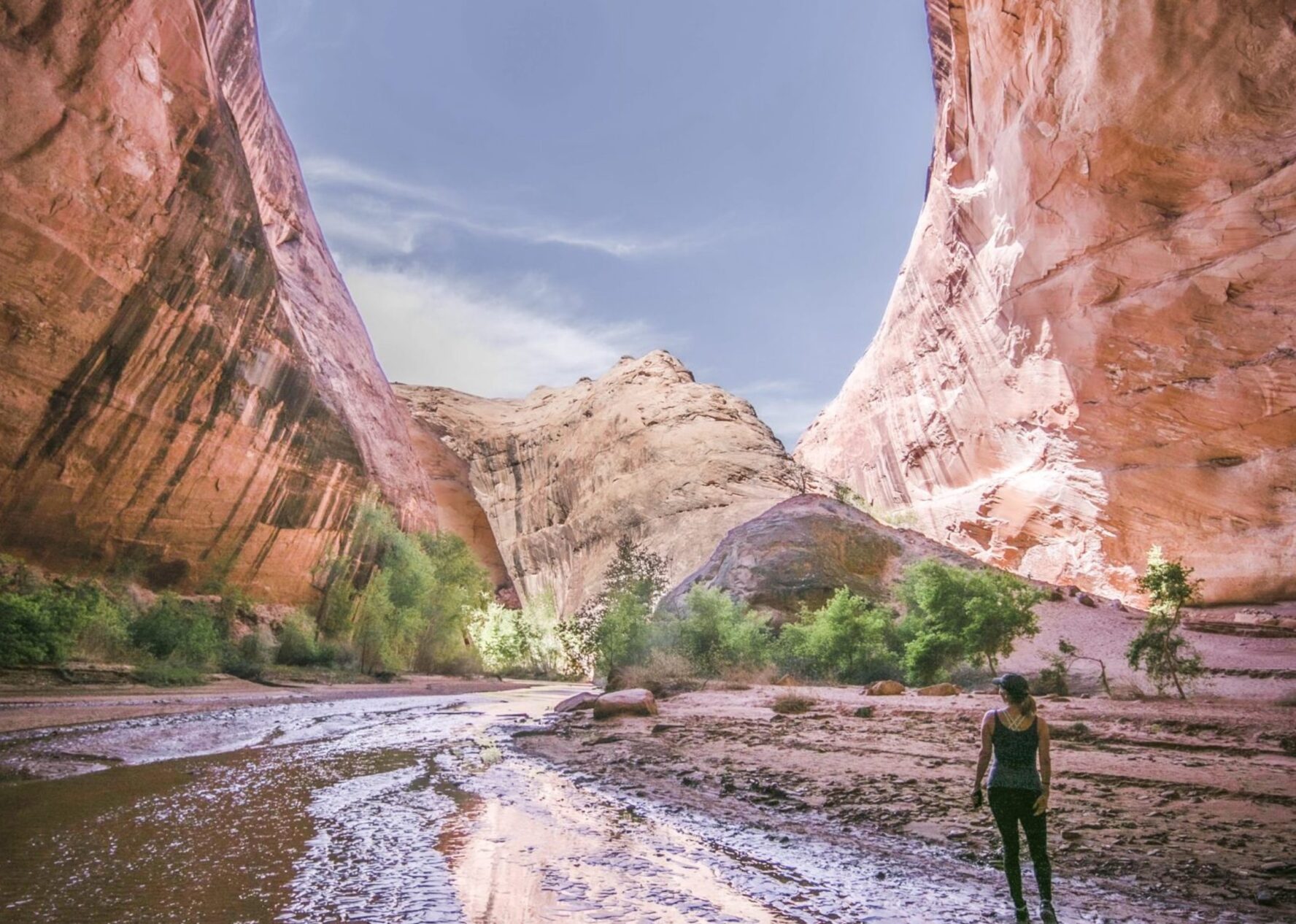 A stream winding between large sandstone rock formations and a backpacker at one of its banks, Coyote Gulch, Escalante, Southern Utah.