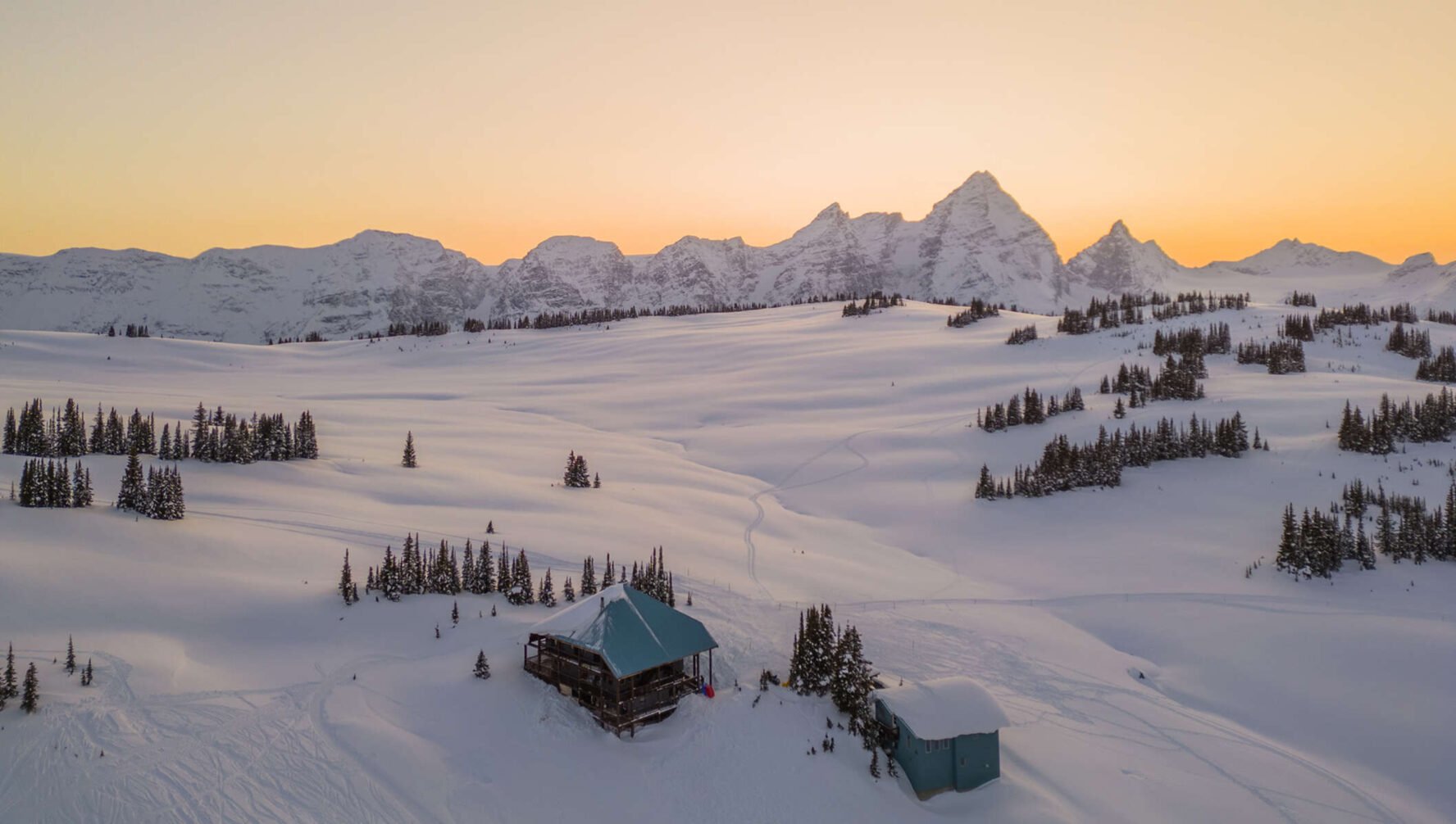 Purcell Mountain Lodge seen from above during sunset, with surrounding mountains in the distance.
