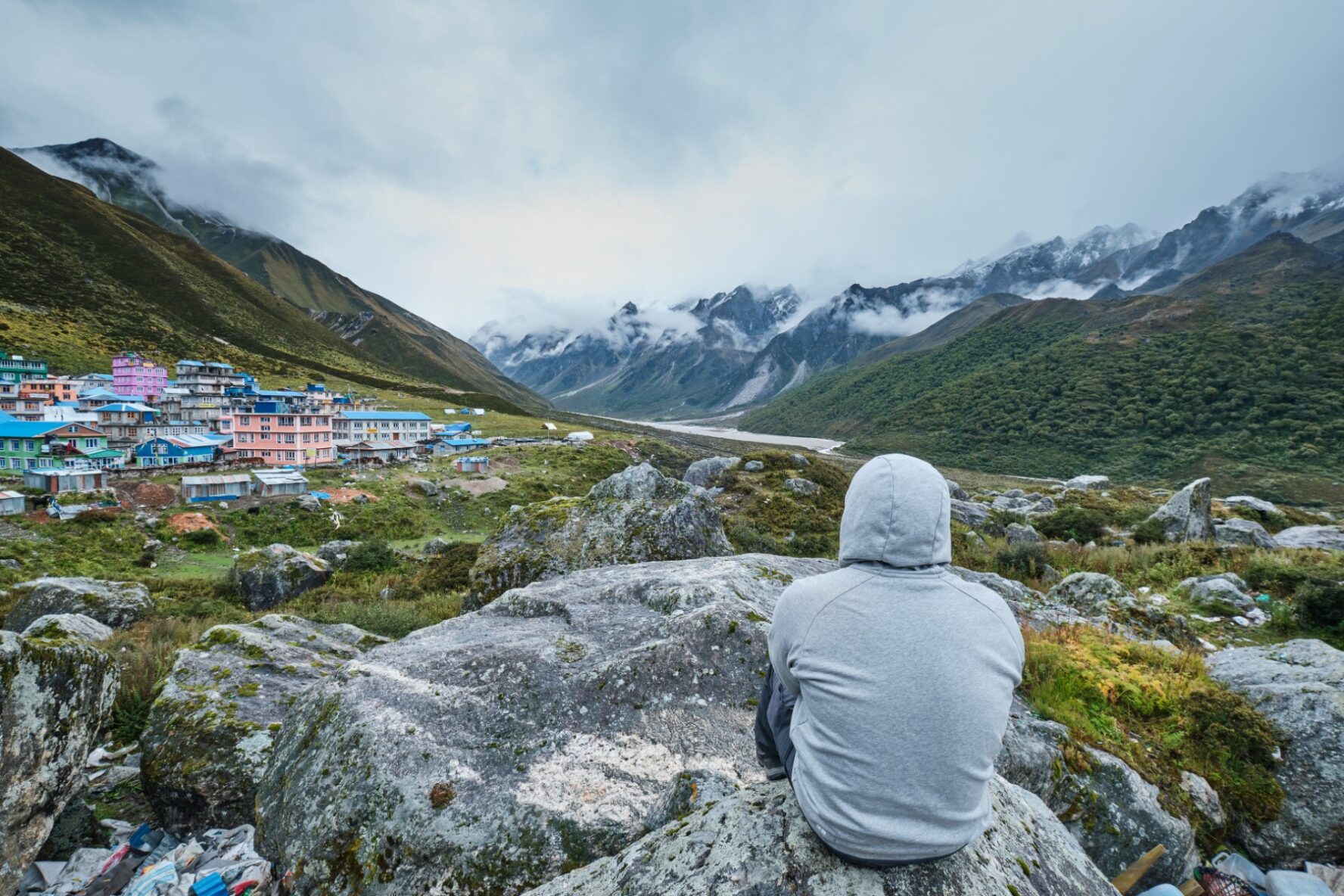 Trekker is sitting on a rock and admiring lush Himalayan landscapes.