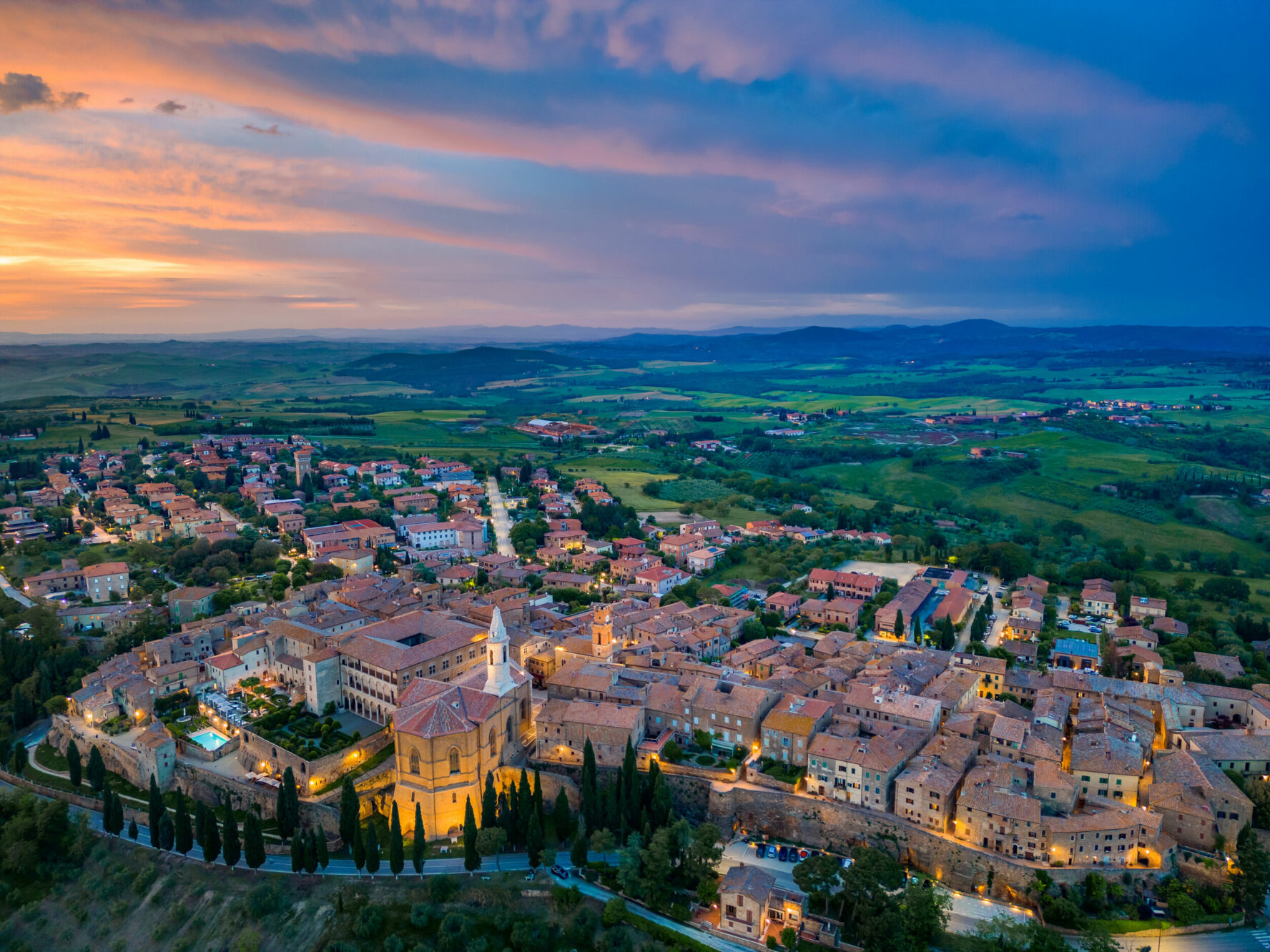 Aerial view of the Tuscan town of Pienza and surrounding patchwork fields, at dusk.