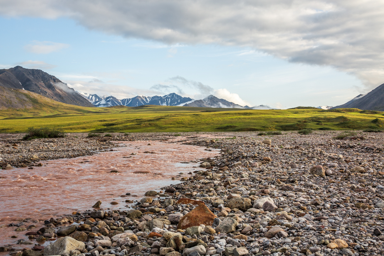Standing alongside a storm swollen river looking across the arctic tundra with its permafrost palsas towards the remote mountains of the Gates of the arctic National Park. Galbraith Lake, Alaska
