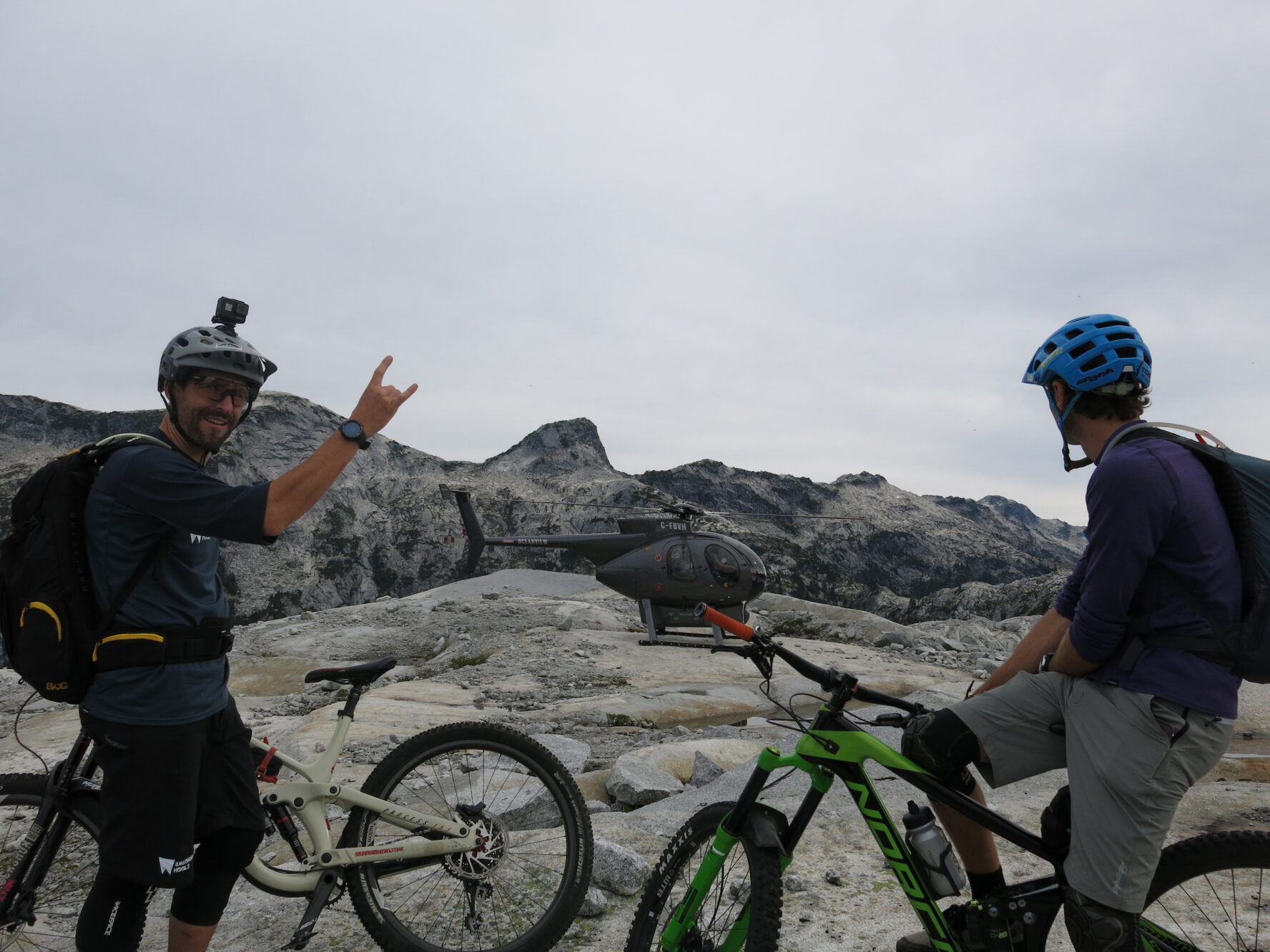 Mountain bikers in BC’s Coast Mountains posing beside a black helicopter.