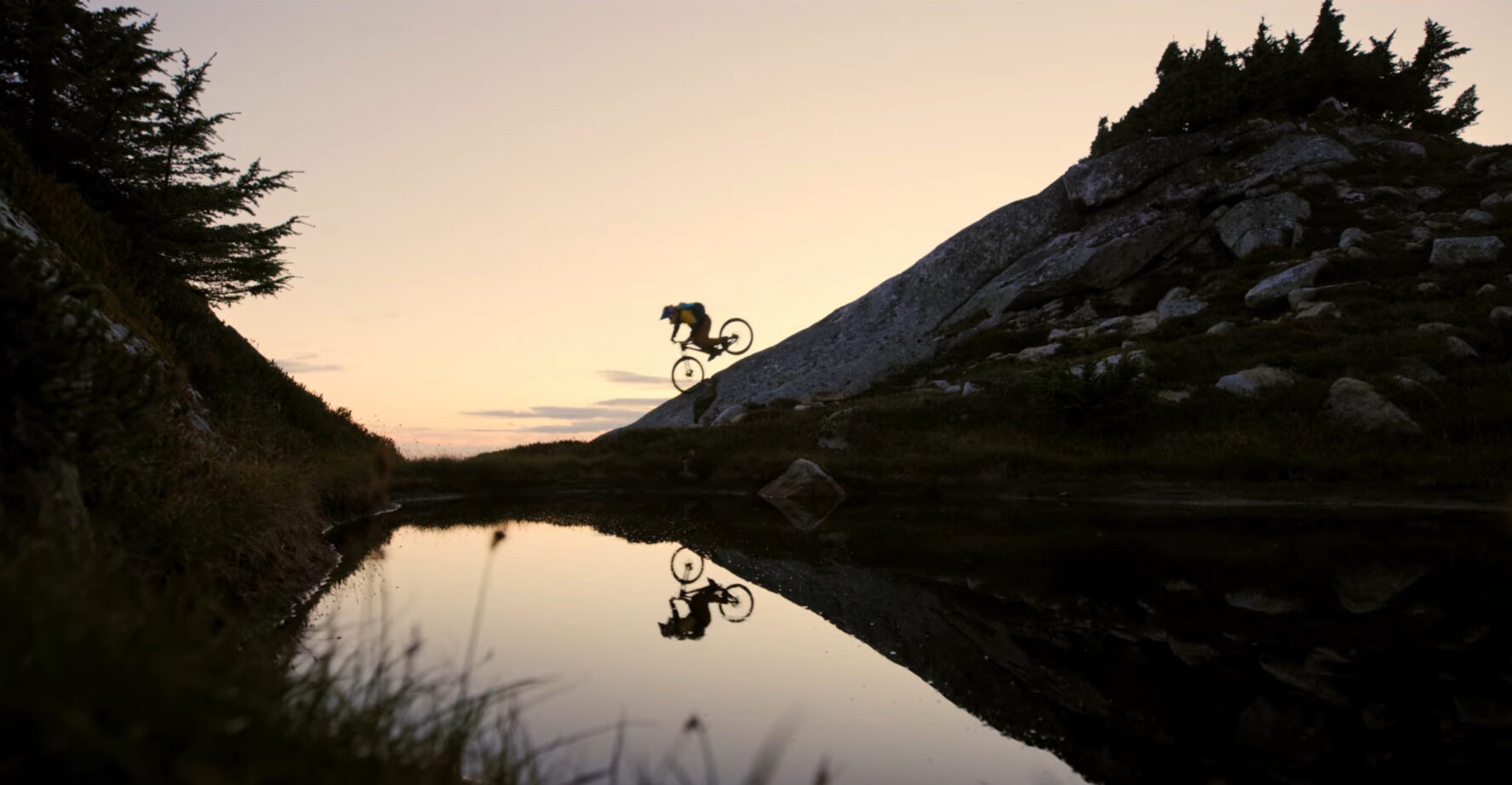 Mountain biker’s silhouette reflected in a small lake near a base camp for a heli-accessed MTB tour in BC’s Coast Mountains.