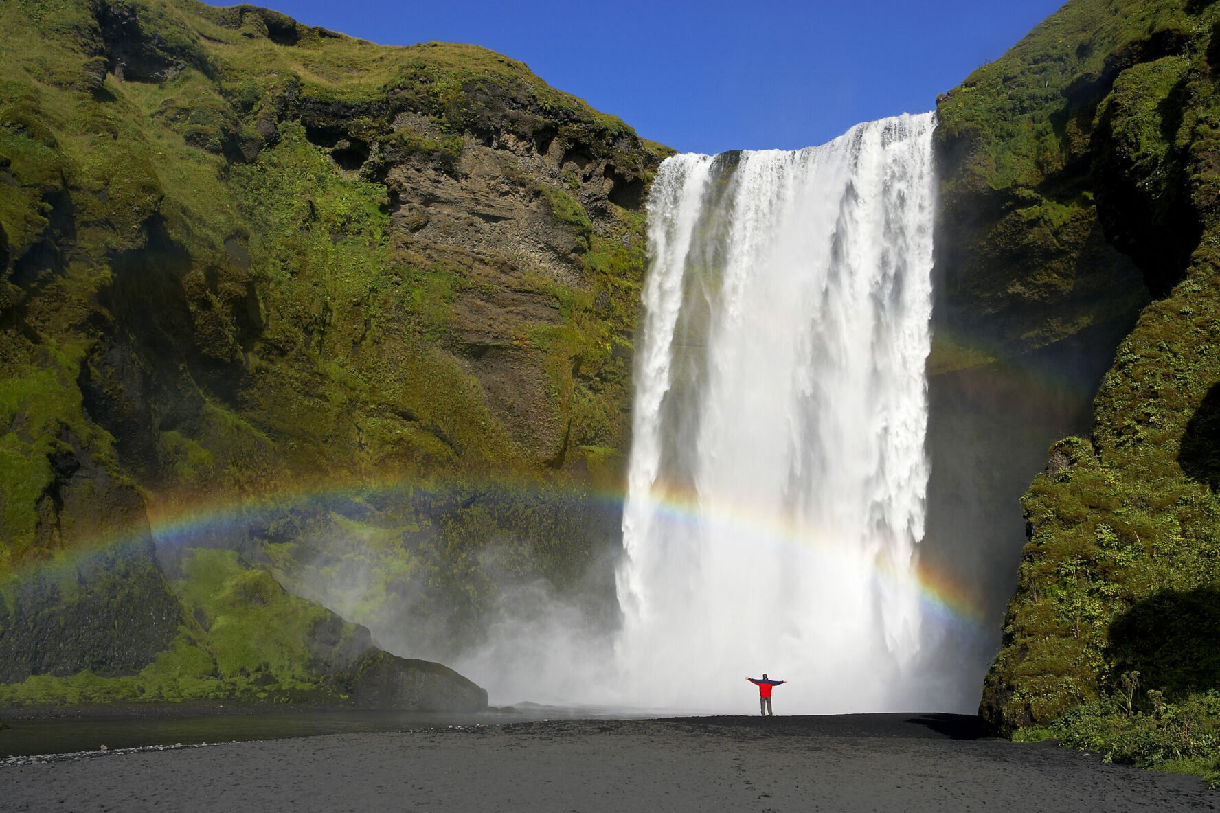 Hiker in front of Skogafoss, Iceland’s largest waterfall and the trailhead of the Fimmvorduhals trail.