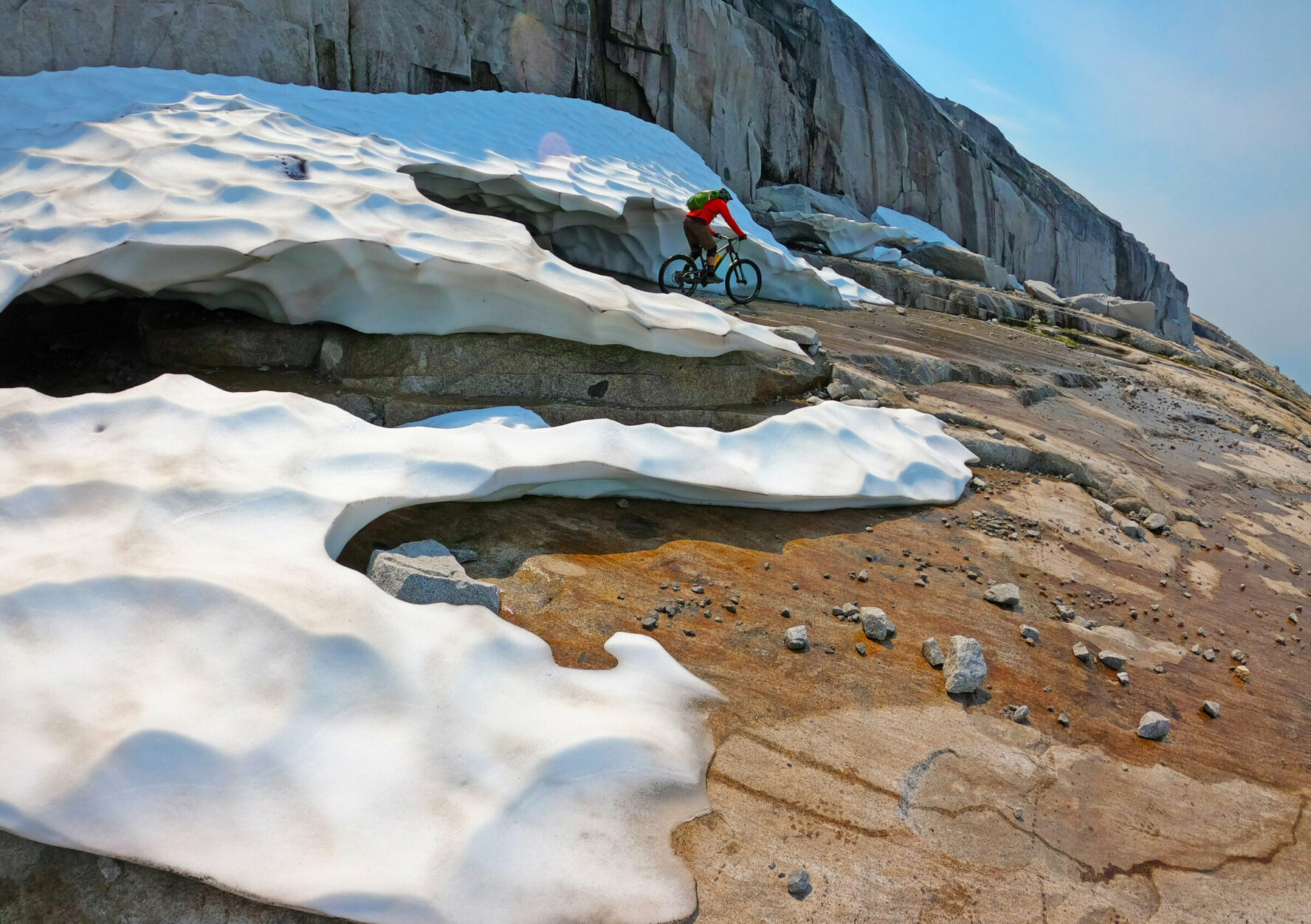 Mountain biker riding beside small glaciers in BC’s Coast Mountains.