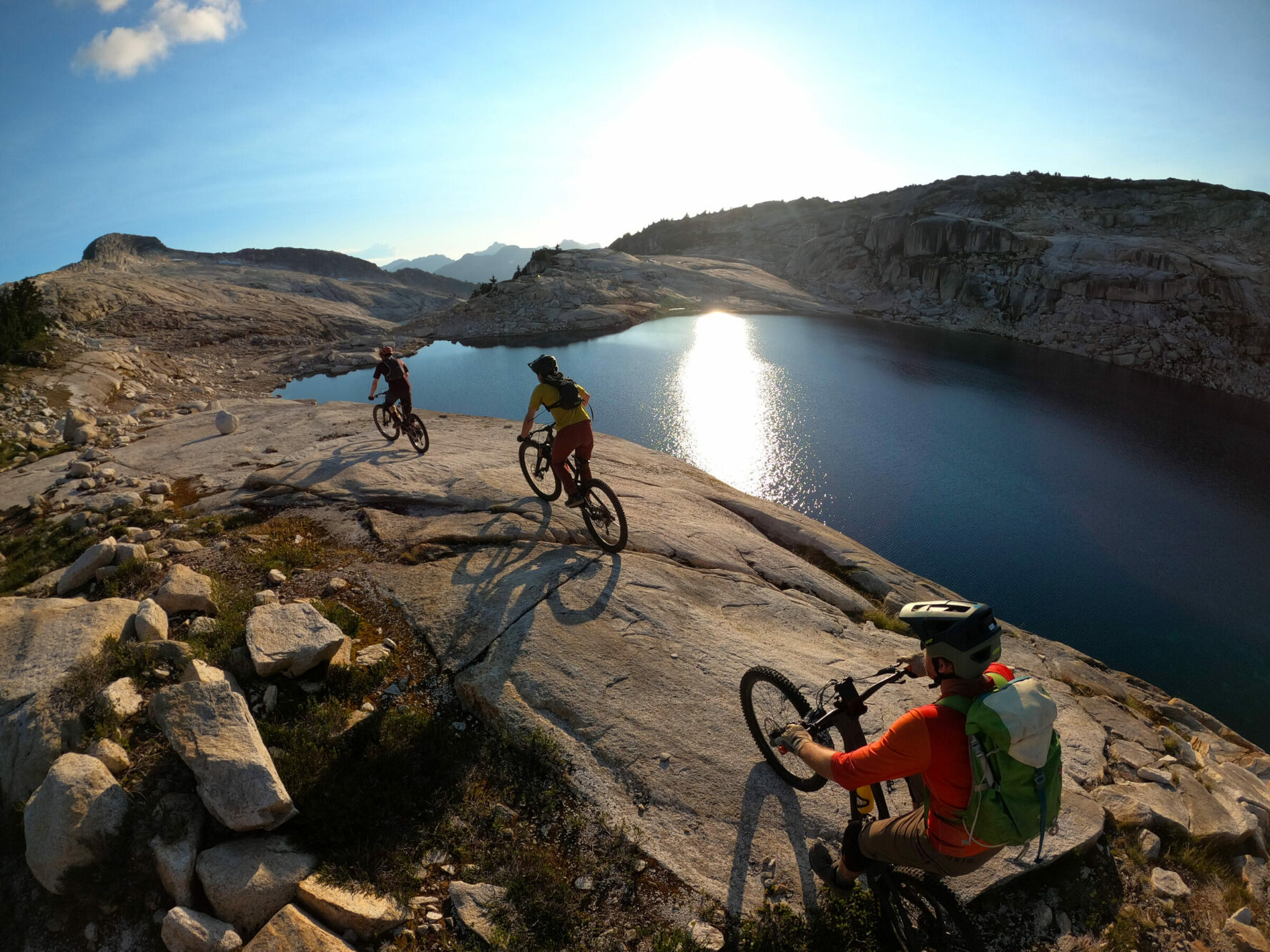 MTBers riding beside a lake in BC’s Coast Mountains during the sunrise.
