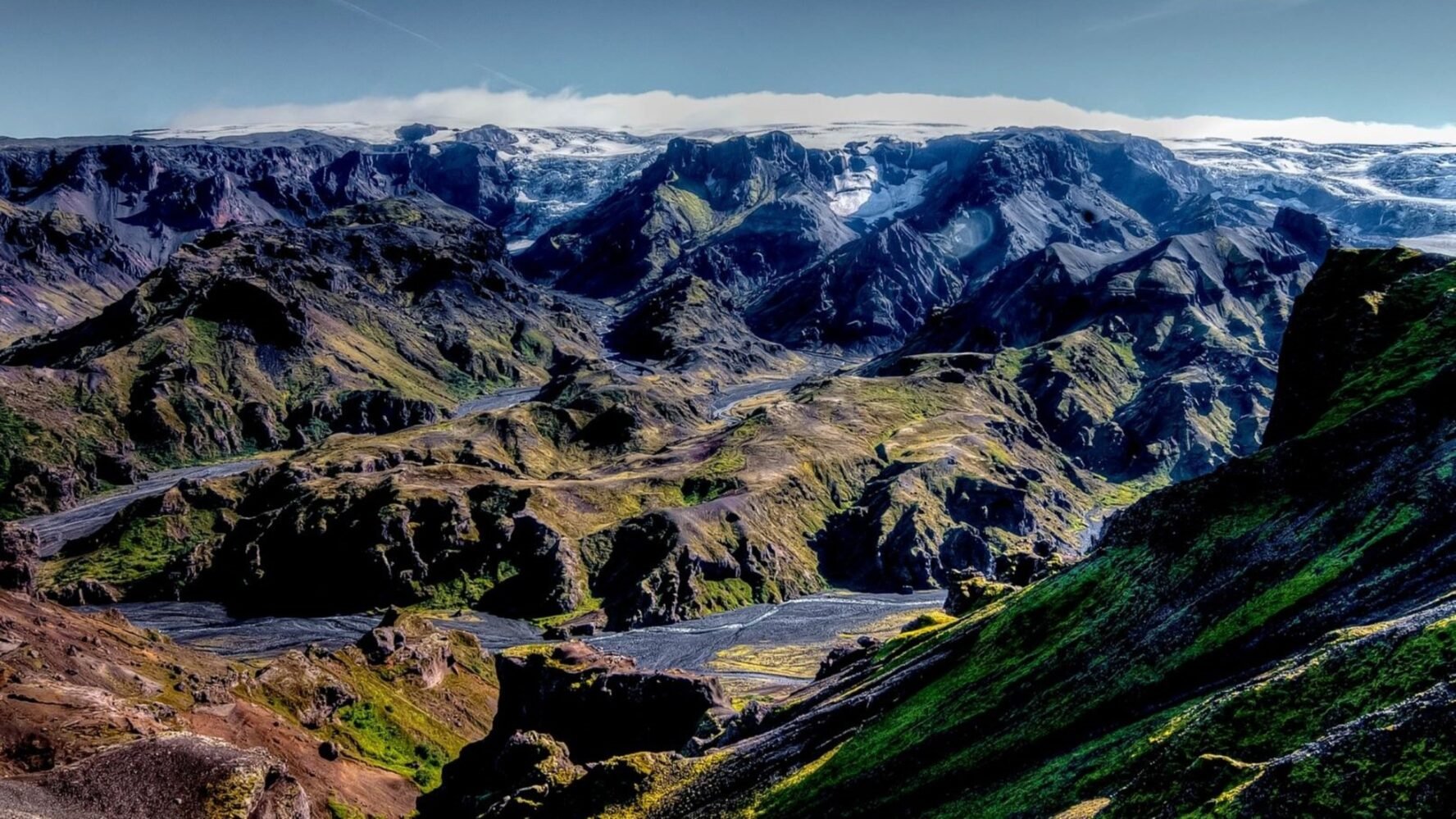Surreal landscape in Thorsmork, with moss-covered mountains and a large canyon at the bottom of which is a river bed with a braided river.