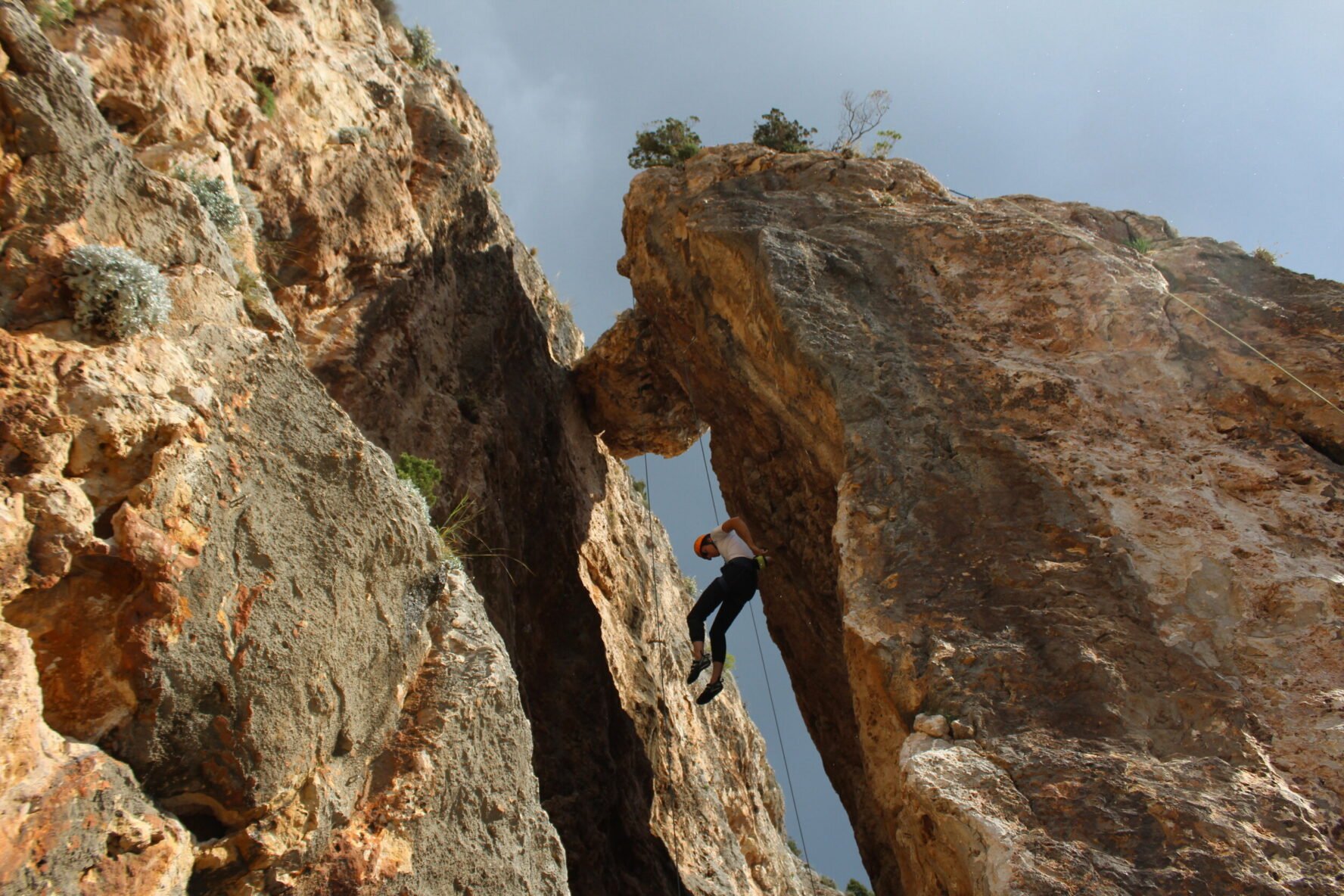 Climber ascending a steep rock face with a natural arch at the top