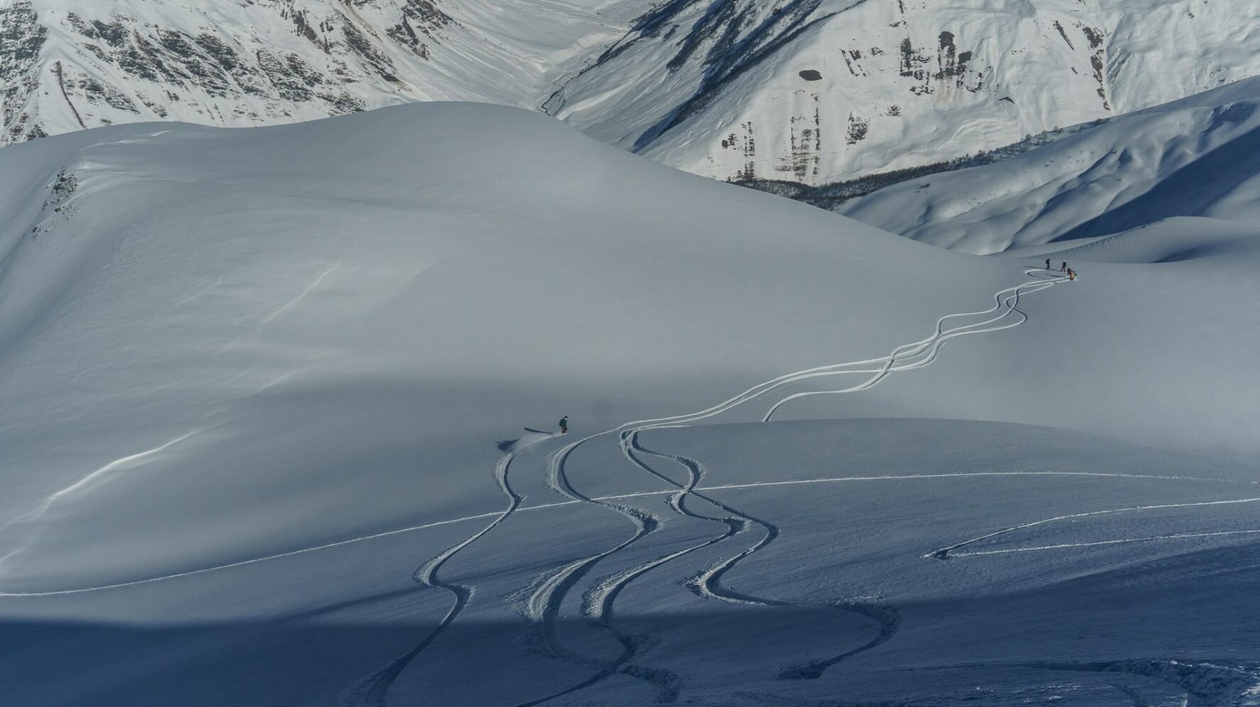 Fresh ski tracks winding down a snowy mountainside in Svaneti with skiers in the distance