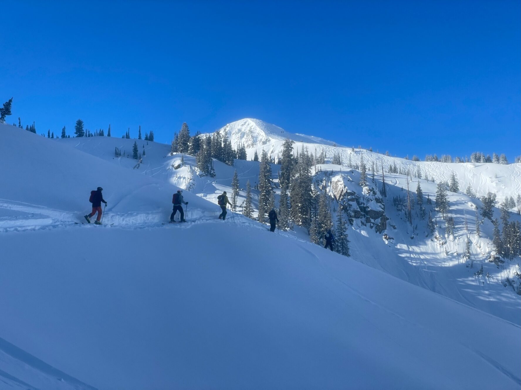 A group of skiers ascending a snowy slope with a mountain peak in the background