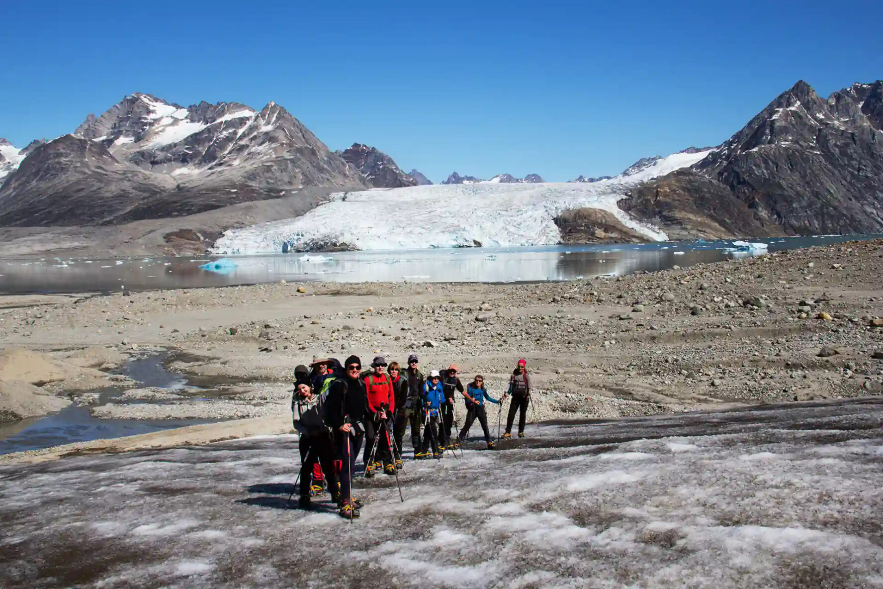 A group of hikers on a glacier in Greenland, with a large glacier and mountains in the background