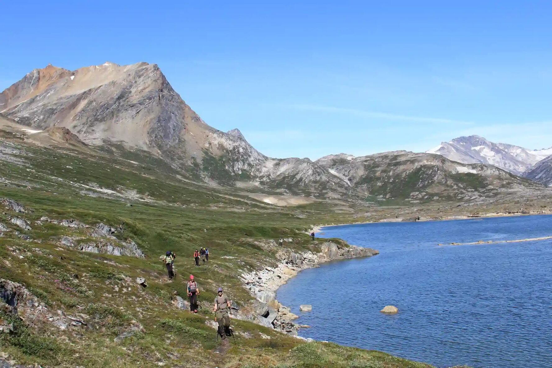 Hikers walking along a shore in the mountainous Greenland landscape