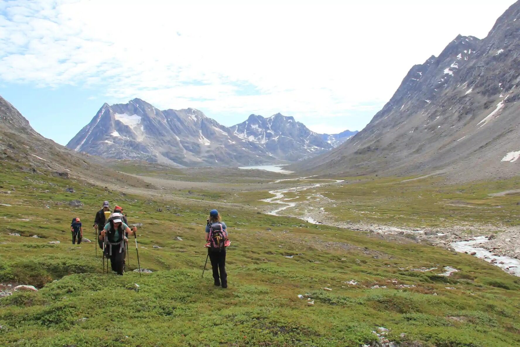 Hikers walking through a valley surrounded by mountains in Greenland