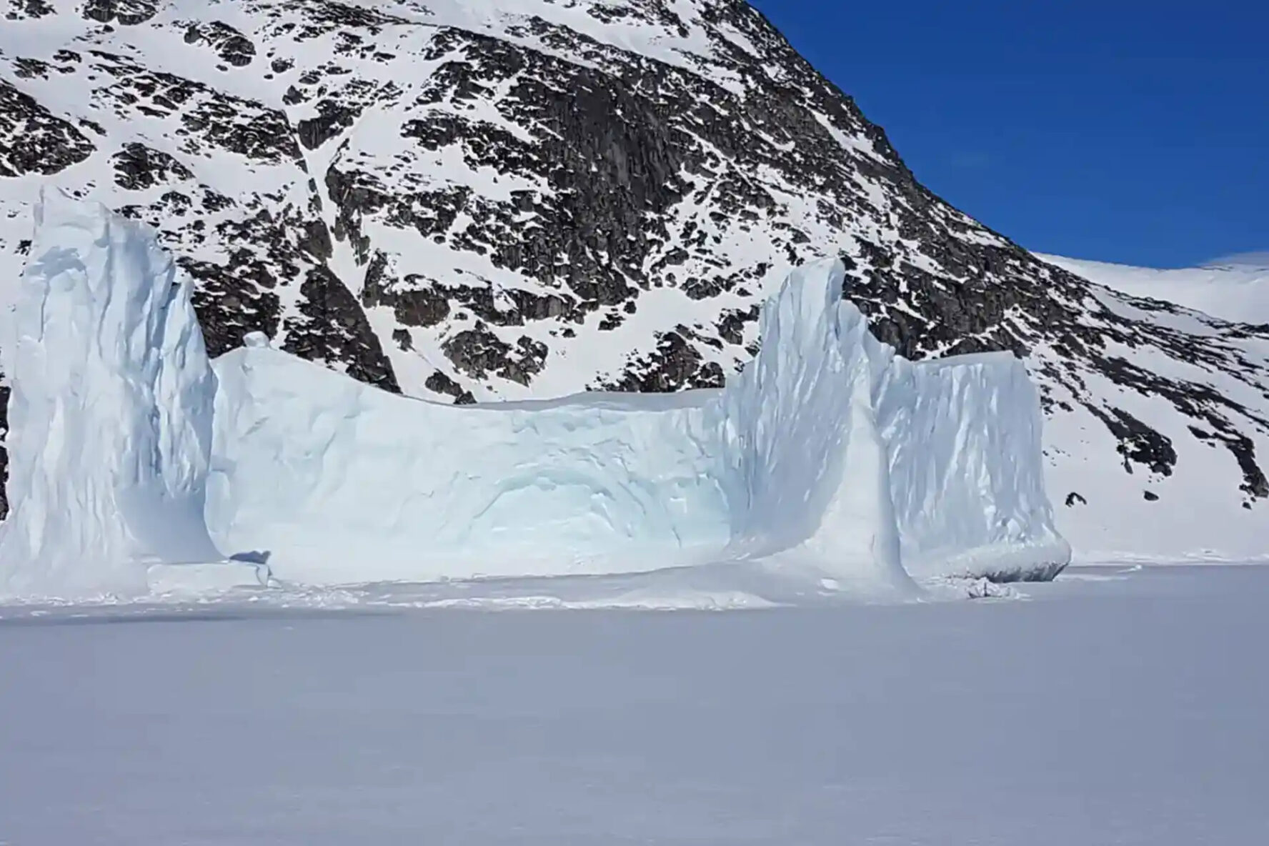 A large iceberg in East Greenland with a snowy mountain in the background
