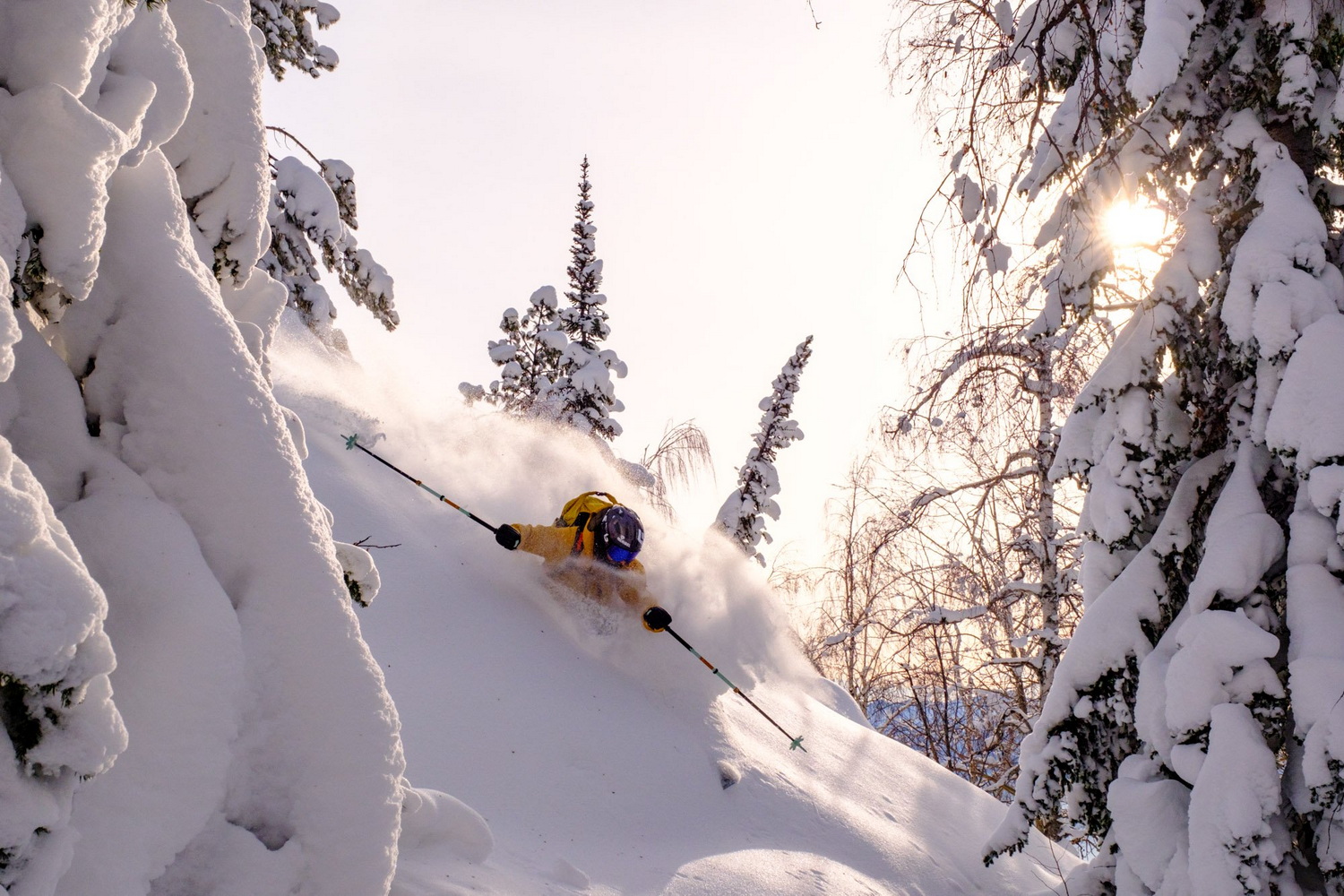 A skier carving down a steep slope in the Altay Mountains, with snow spraying up around him