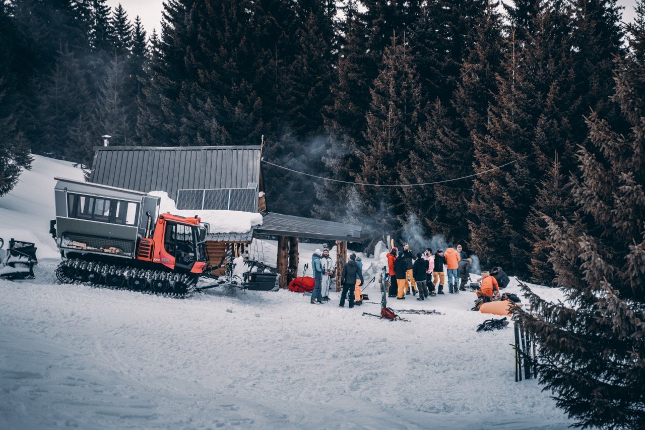 Skiers and a snowcat near a mountain hut