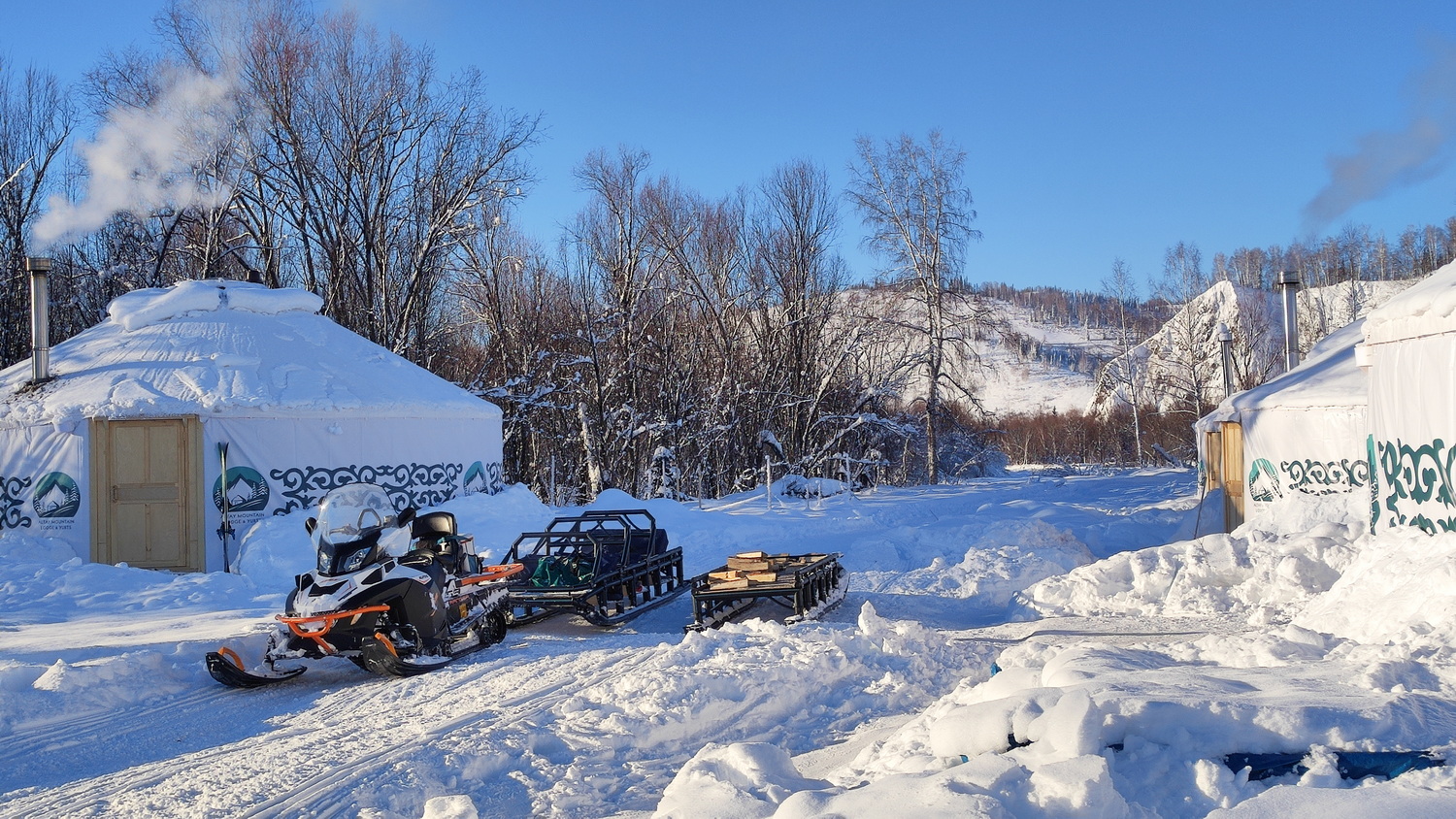 A snowmobile parked between the yurts at Altay Mountain Lodge
