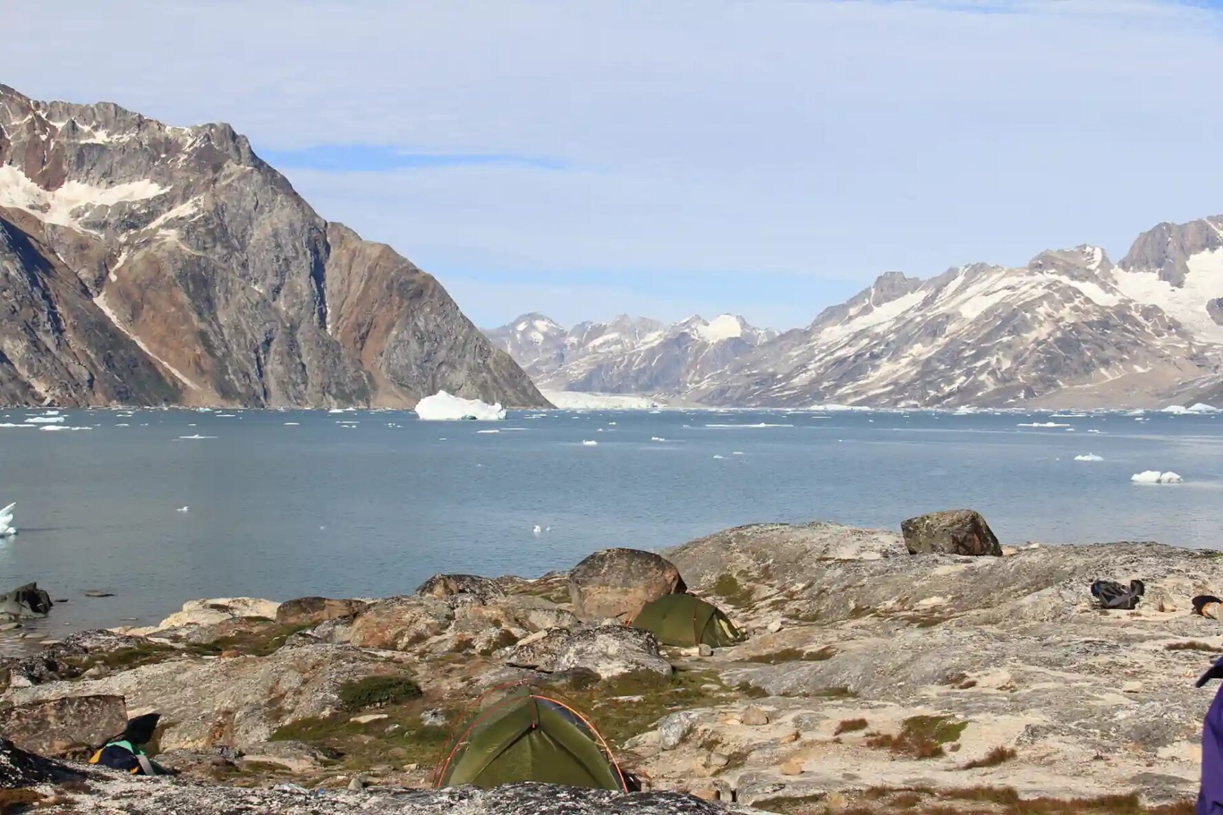 Tents pitched on a rocky shore overlooking a glacier-filled fjord