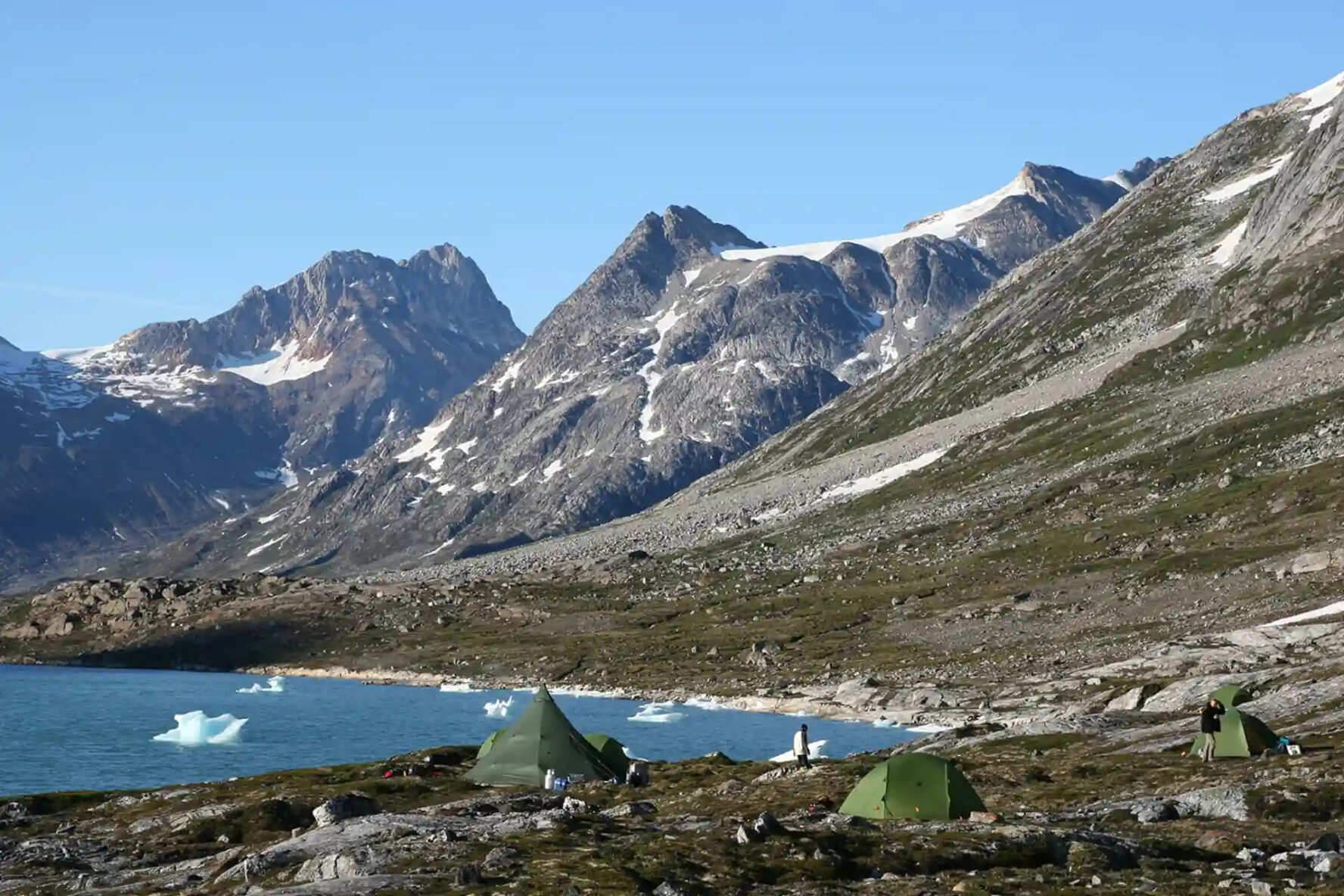 Three green tents pitched on a rocky shore