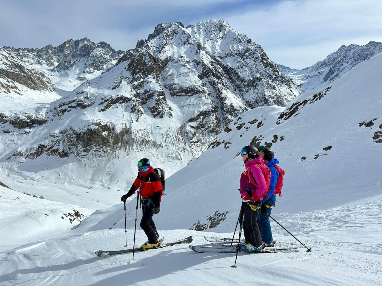 Three skiers stand on a snowy mountaintop in Svaneti, admiring the view