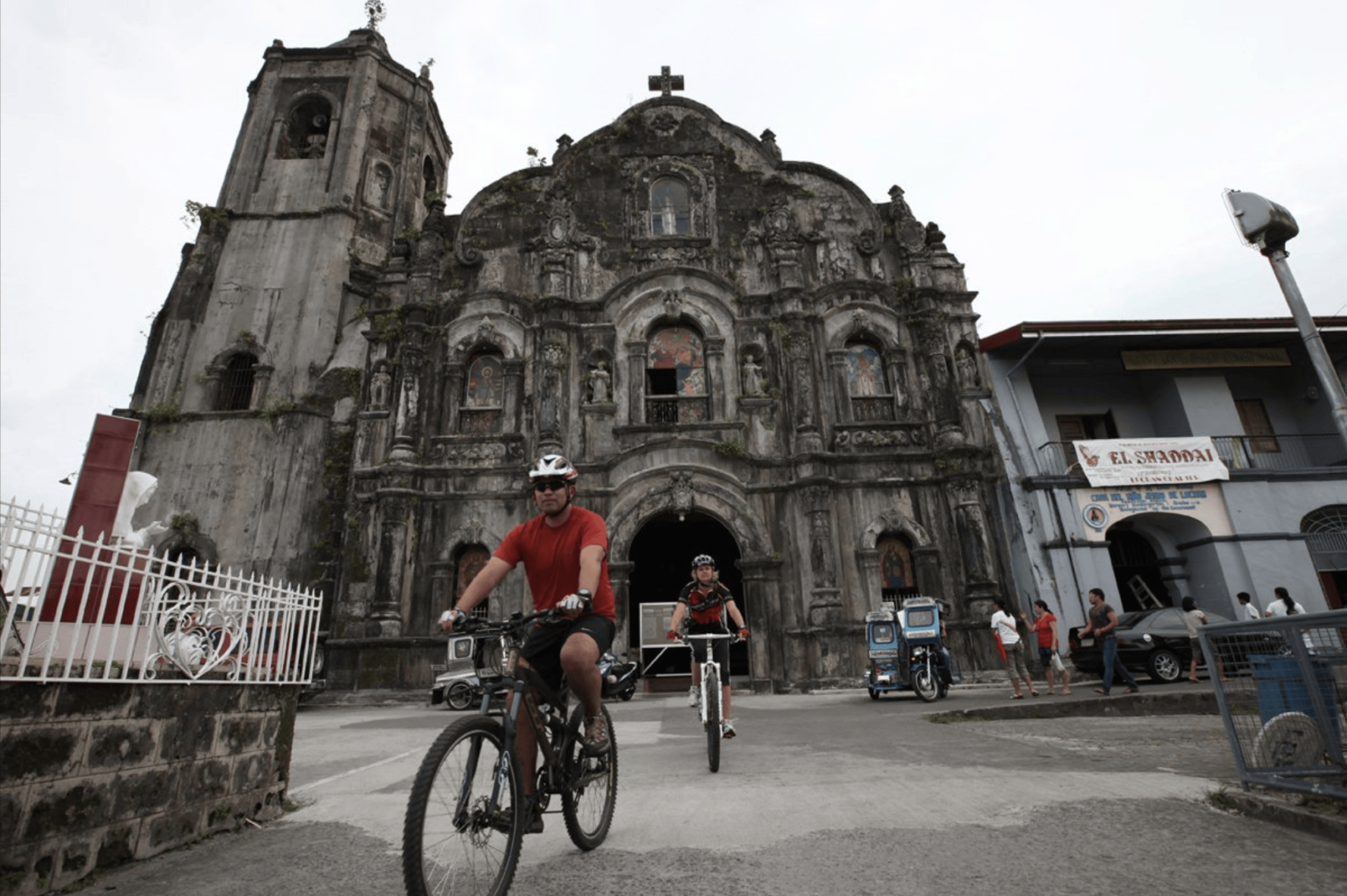 Two cyclists riding bikes in front of a historic church in the Philippines
