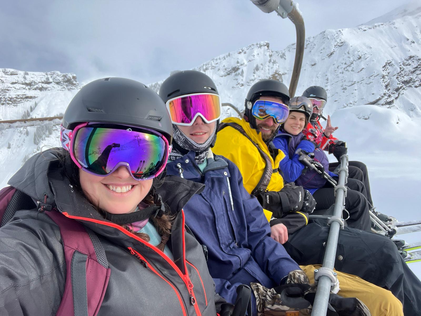 Five skiers on a chairlift with snowy mountain background