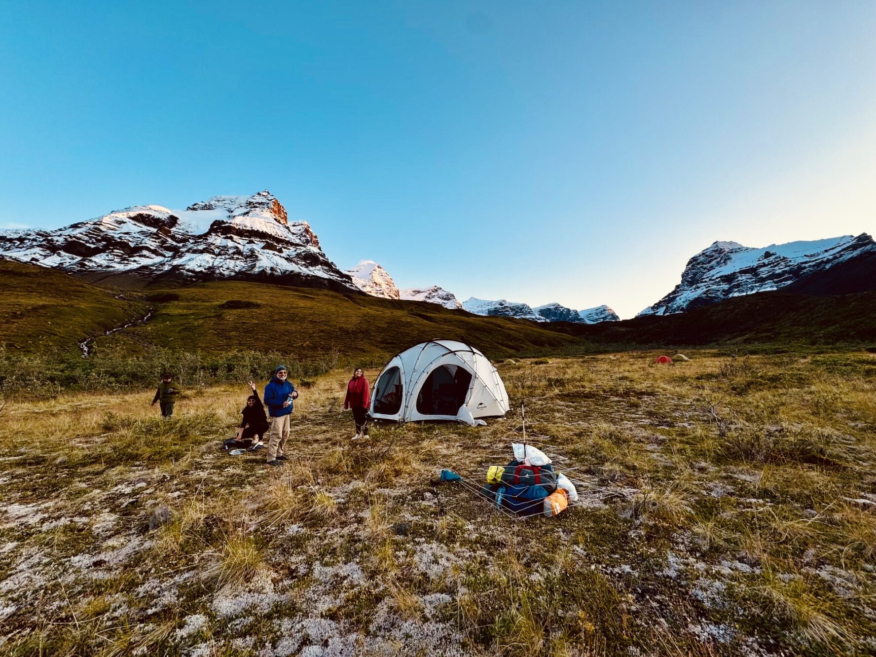 Hikers camping in mountain terrain with a white tent and backpacks