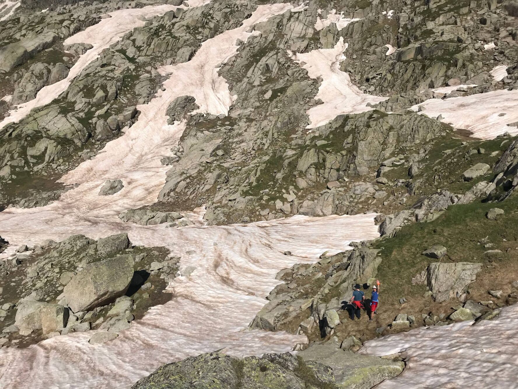 Hikers on a mountain trail with glaciers and patches of exposed rock