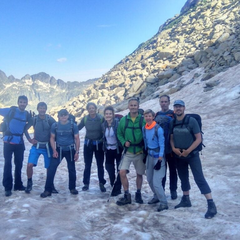Hikers on a snowy mountain trail with rocky landscape in the background