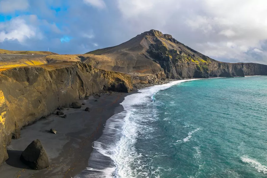 A seaside landscape with dark sand and green hills in Iceland