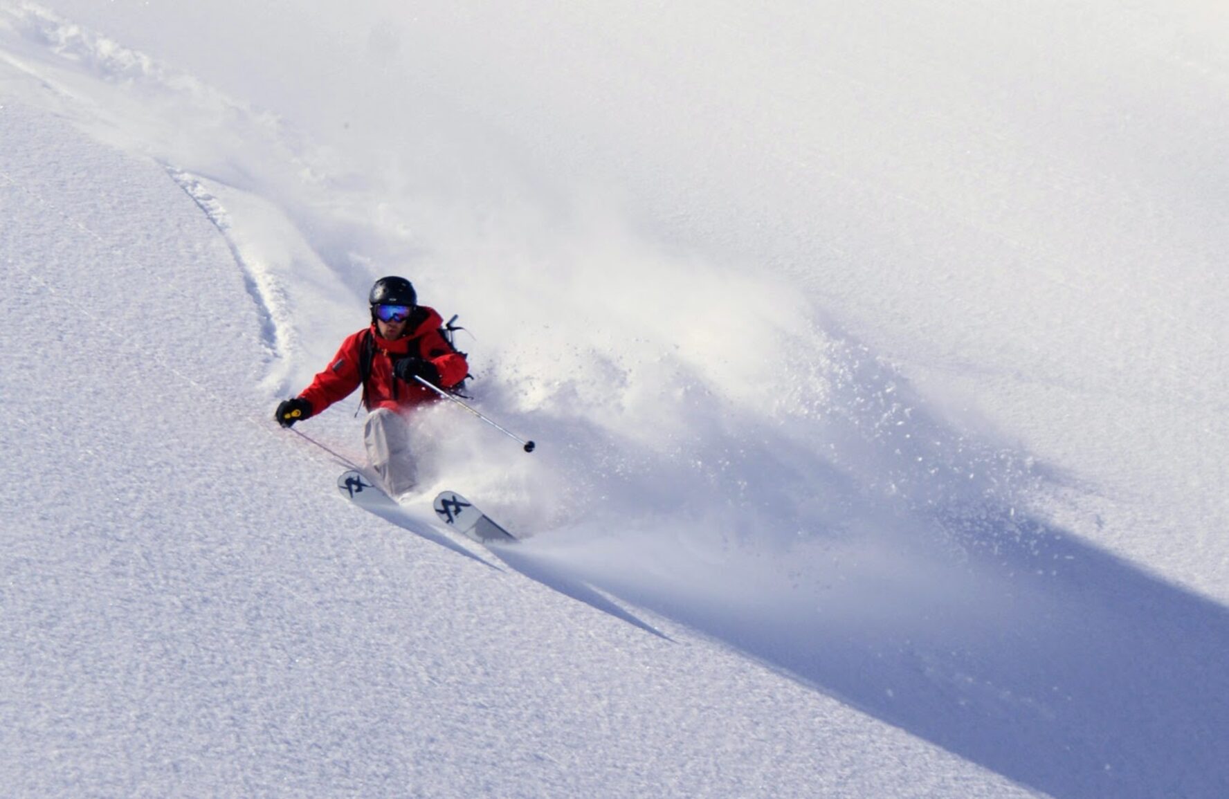 A skier cuts through powder snow on a steep slope