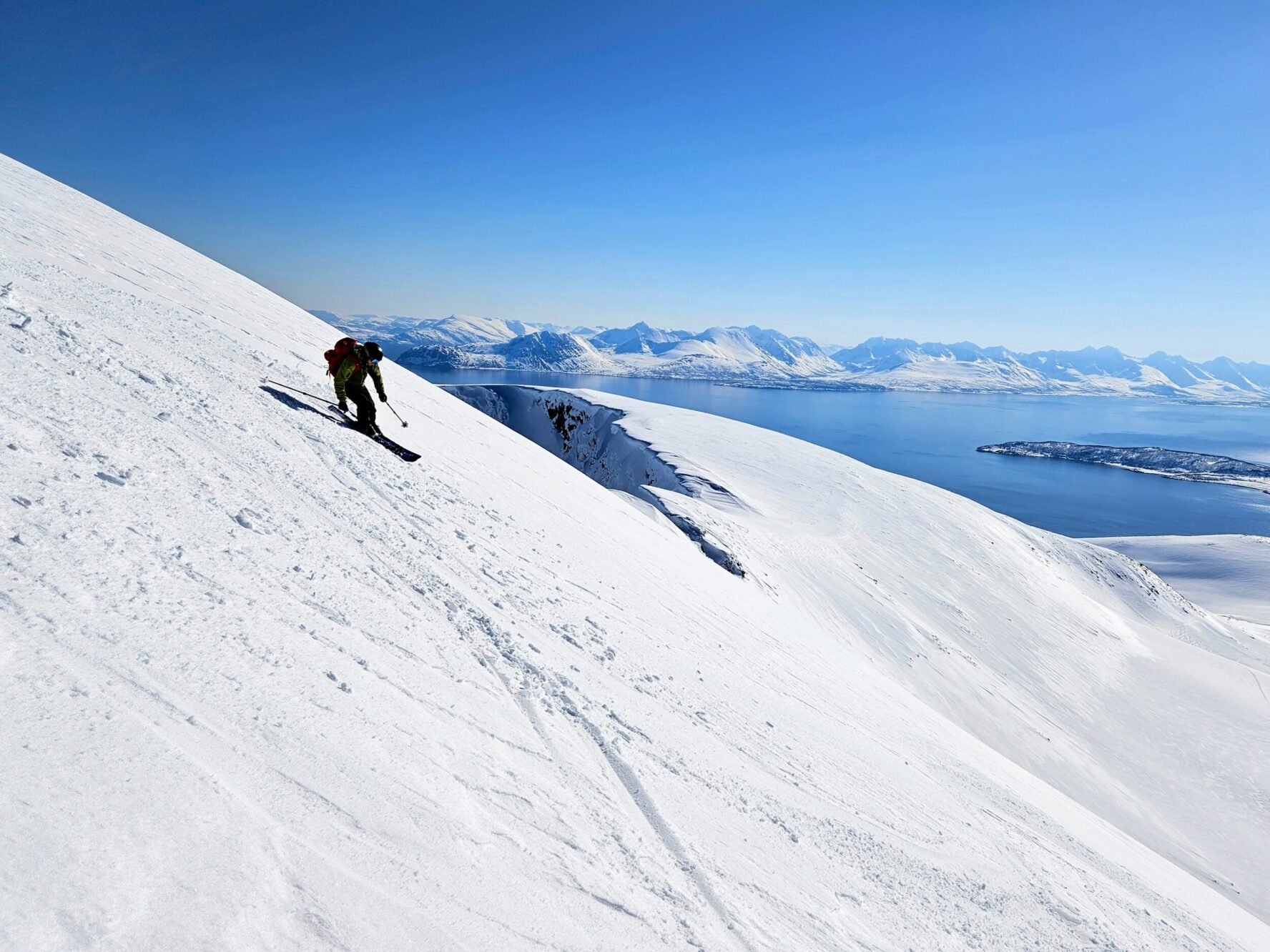 Skier descending a snowy slope in Norway with the sea in the background
