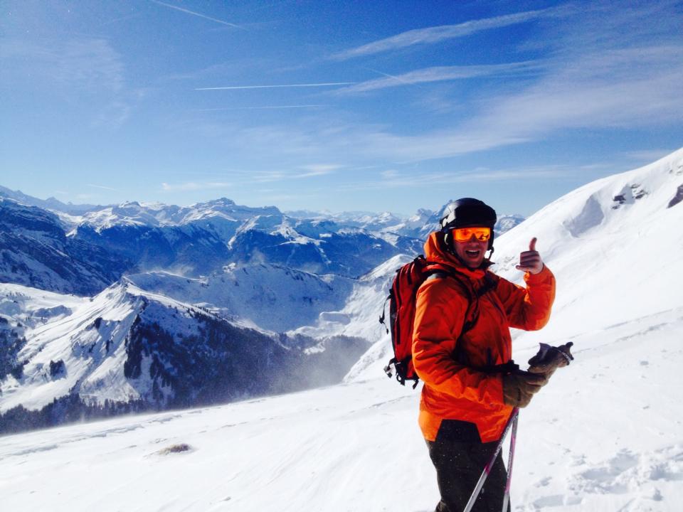 A skier giving thumbs-up on a snowy mountain with clear blue skies