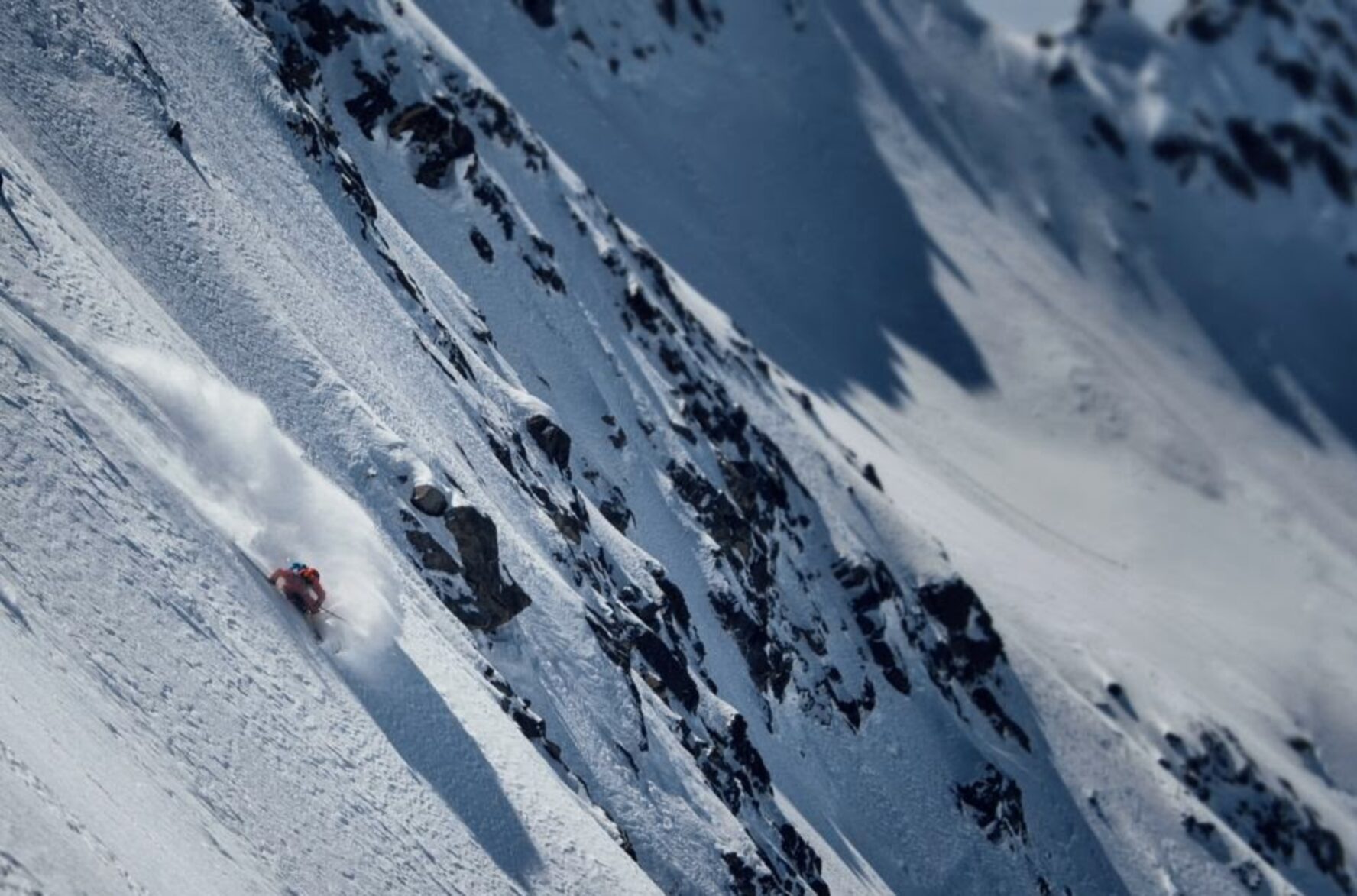 A skier in a red jacket skiing down a steep snowy slope