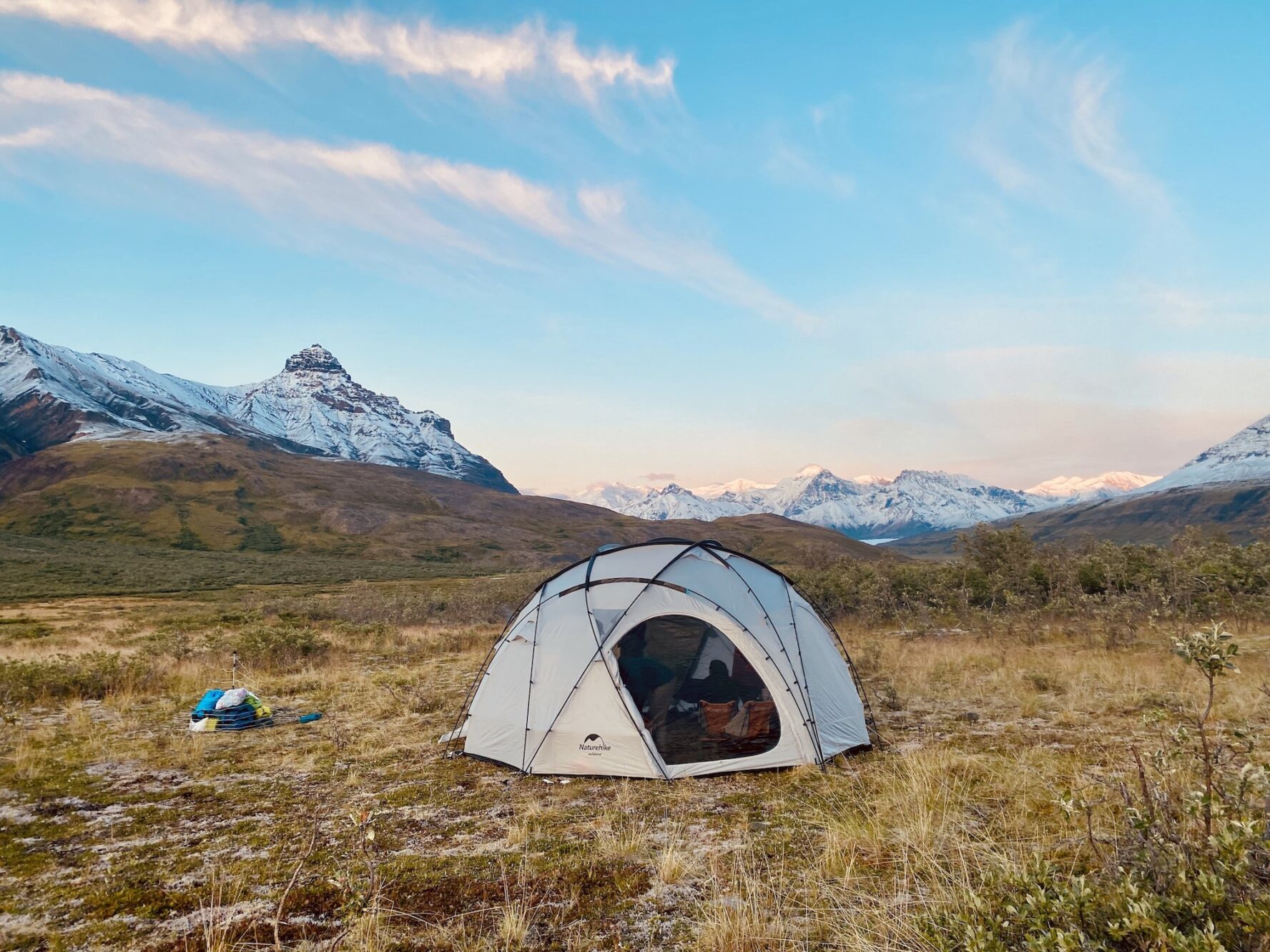 A tent pitched in a field with snow-capped mountains in the background under a clear sky
