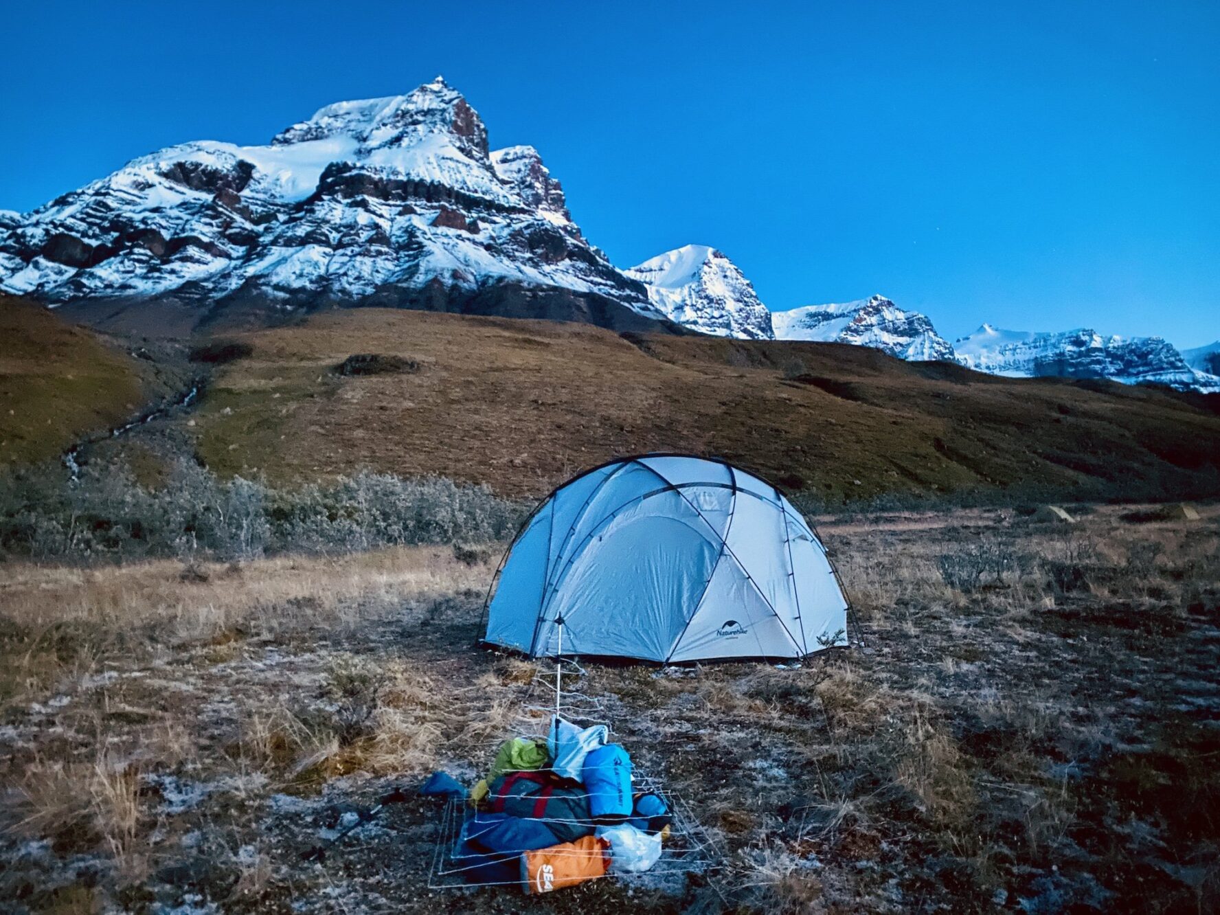 Tent in a wild grassy area with snow-capped mountains in the background at twilight