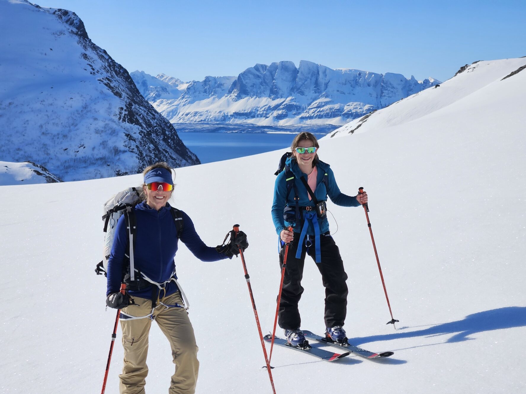 Two skiers smiling and holding ski poles on a snowy mountain slope in Norway