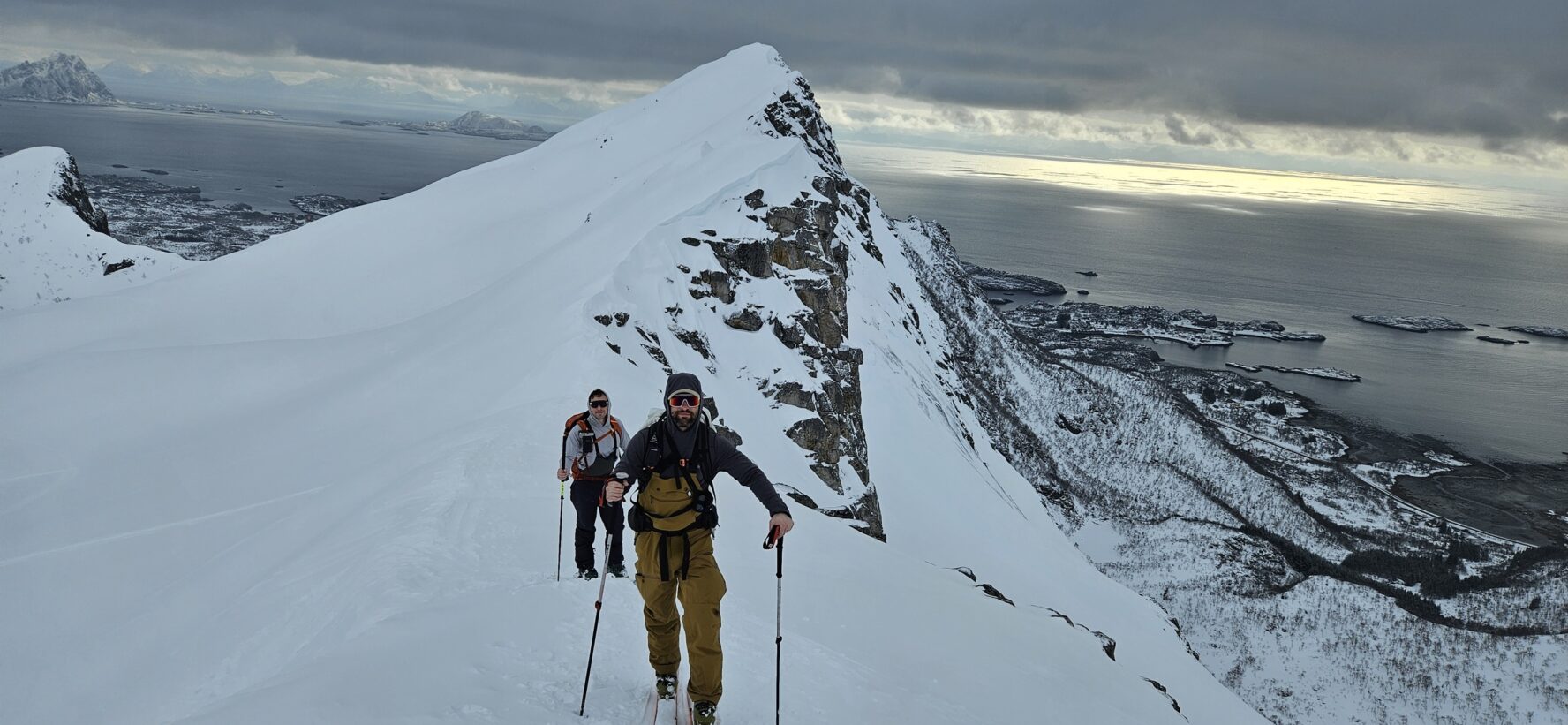 Two skiers on a snow-covered mountain overlooking the sea and islands in Norway