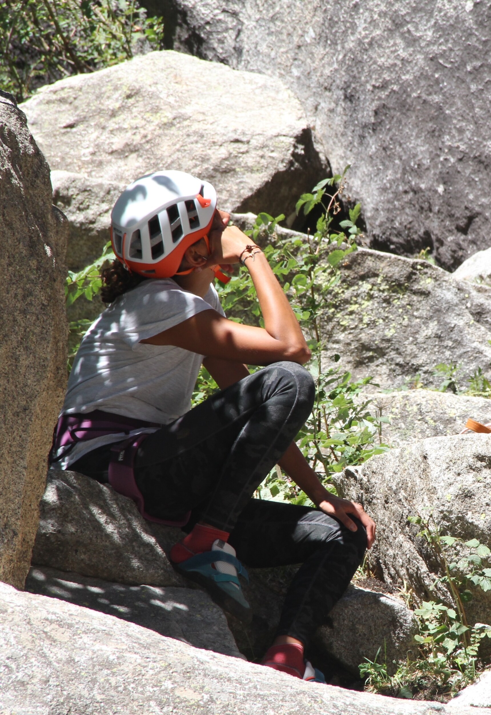 A climber resting on a rock surrounded by boulders and vegetation