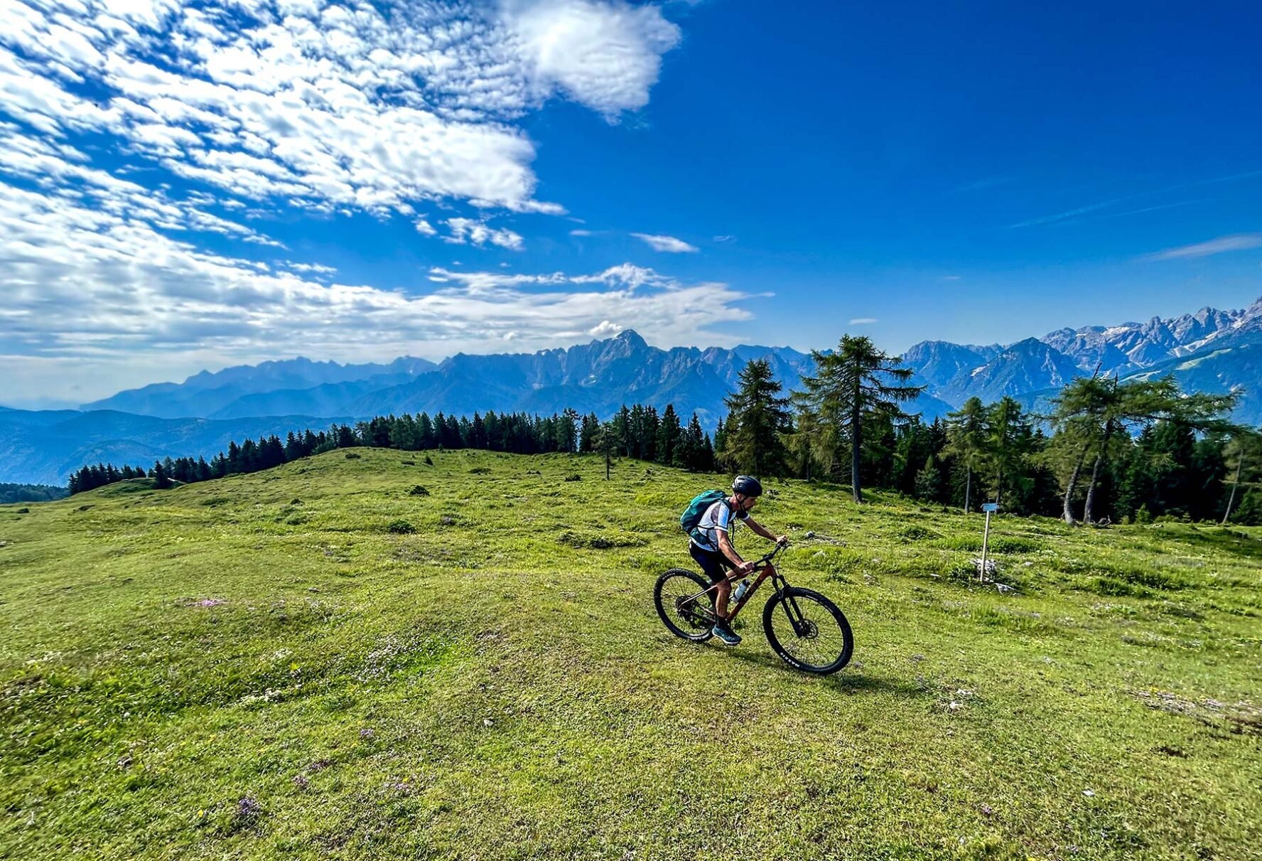 Cyclist riding on grassy hill with the Alps in the background