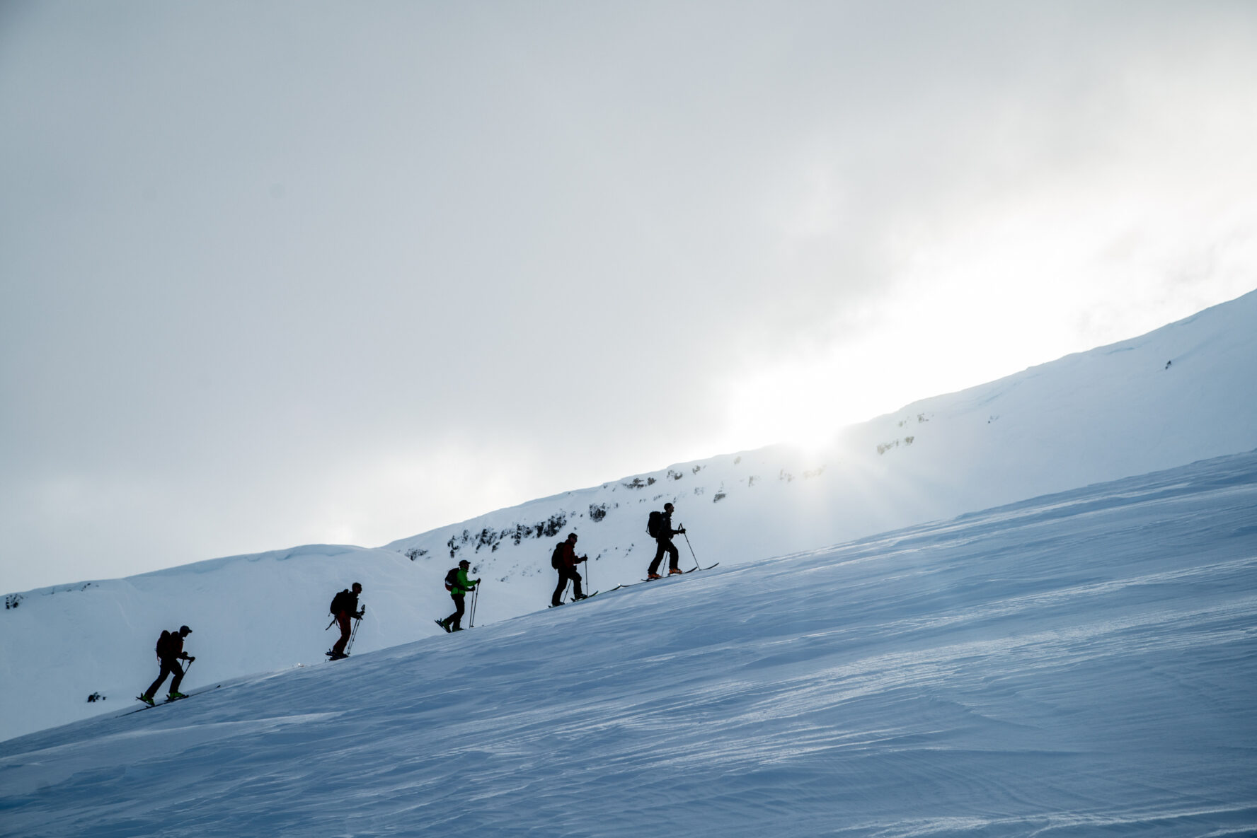 Four skiers ascending snowy slope with the sun shining in the background