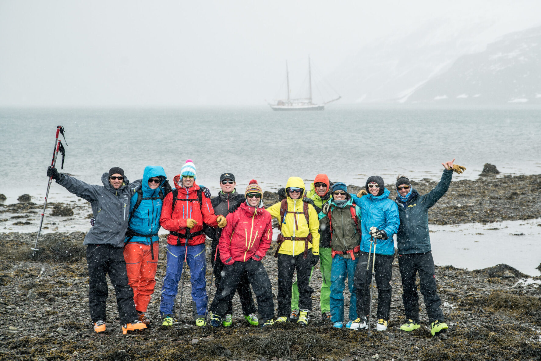 Group of people smiling with a sailboat in the background on a snowy shoreline