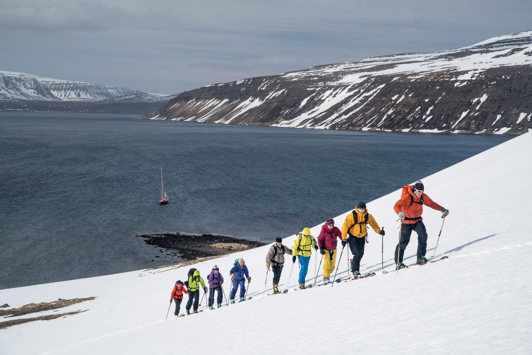 The guide and group ascending a slope with the sailboat, sea and mountains in the background