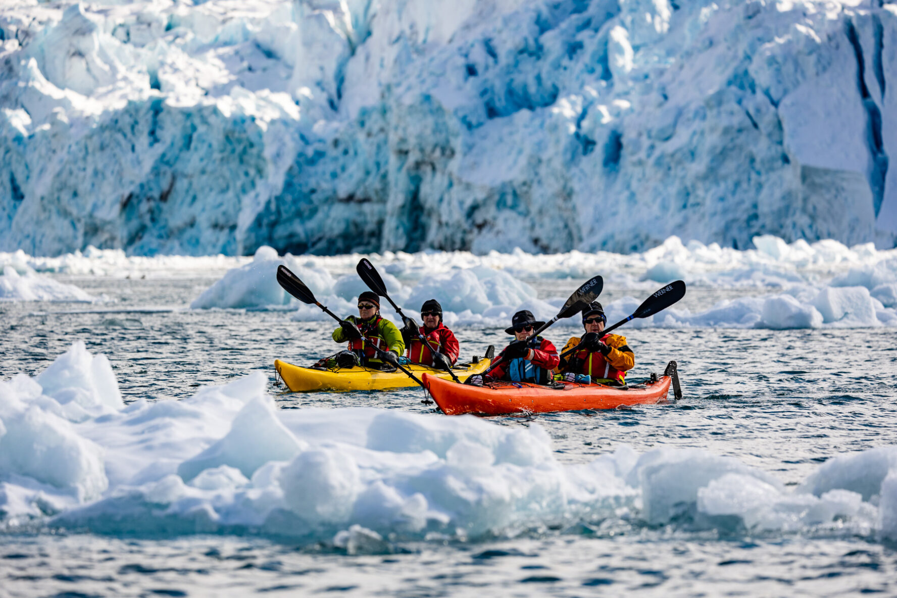 Kayakers paddle among icebergs near a large glacier