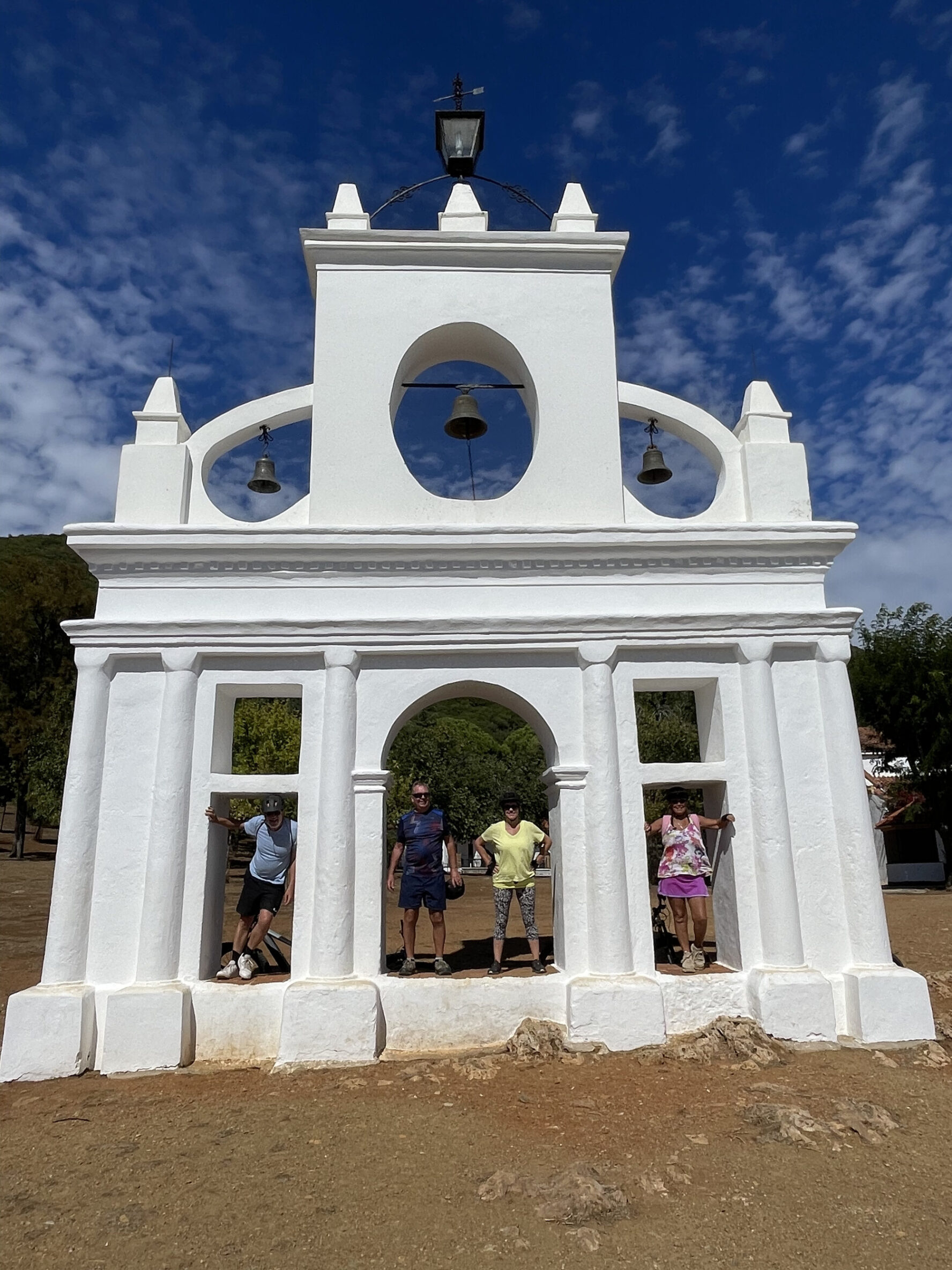 People standing under the arches of the bell tower at La Peña de Arias Montano