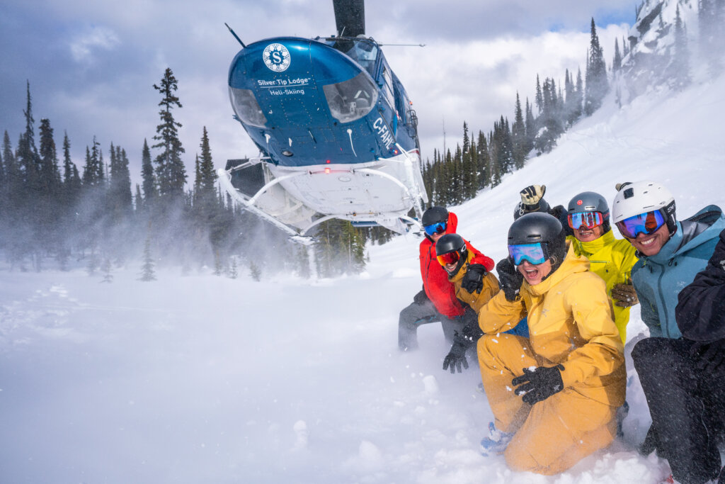 Skiers posing next to a helicopter taking off