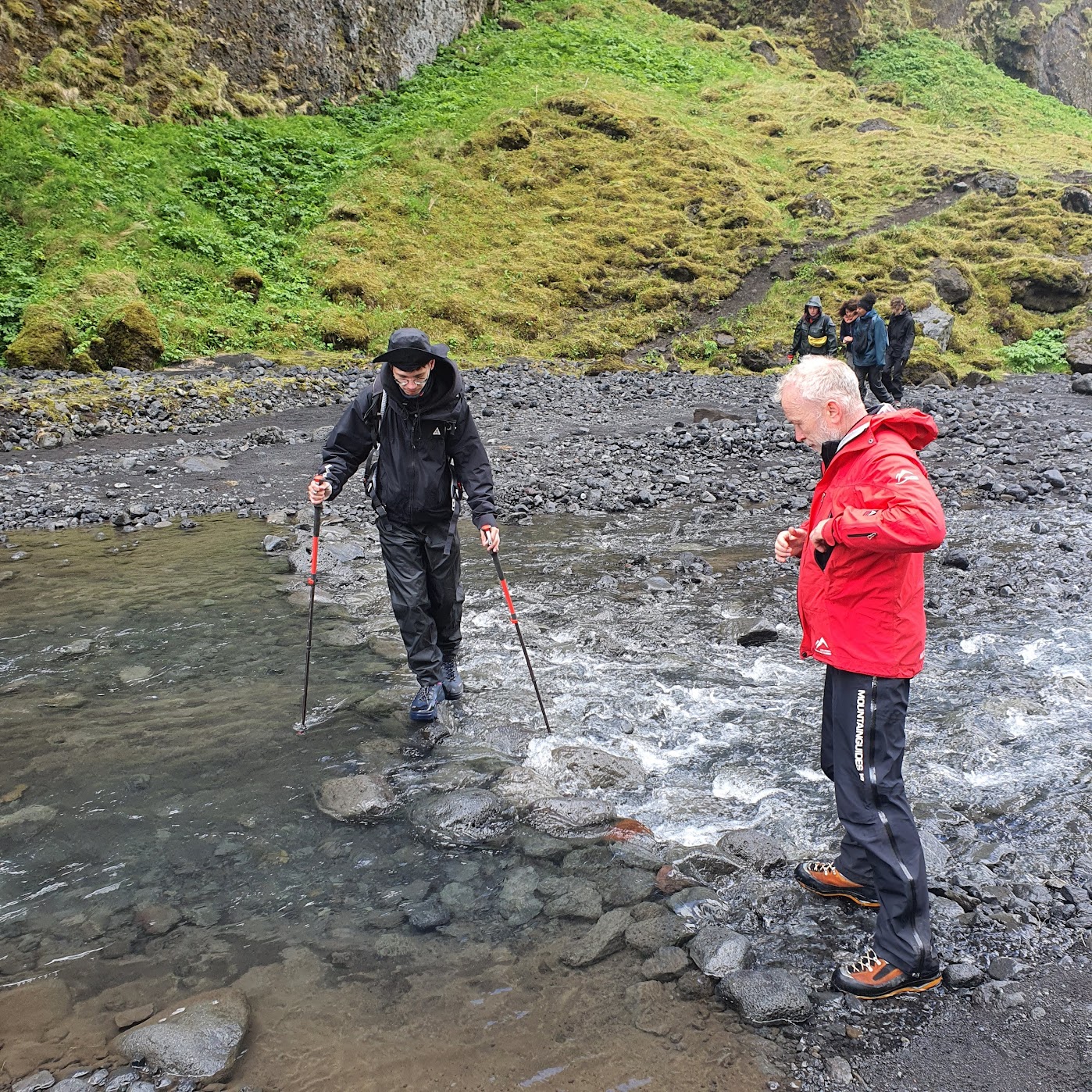 Two hikers crossing a small stream in Landmannalaugar, Iceland