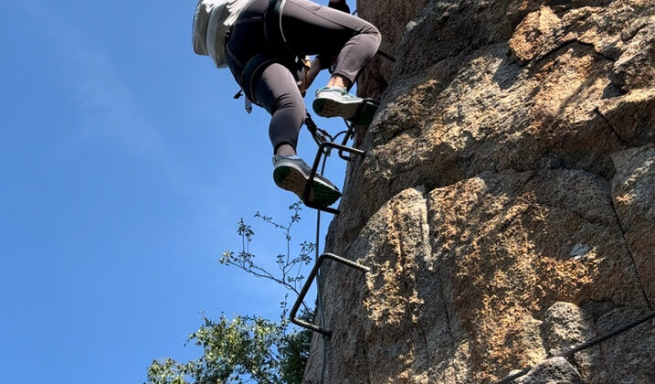 Climbing a steep rock face with via ferrata equipment in Andorra